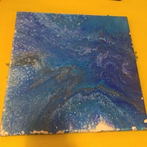 Abstract blue and gold painted canvas with swirling patterns and splatters on a yellow background.