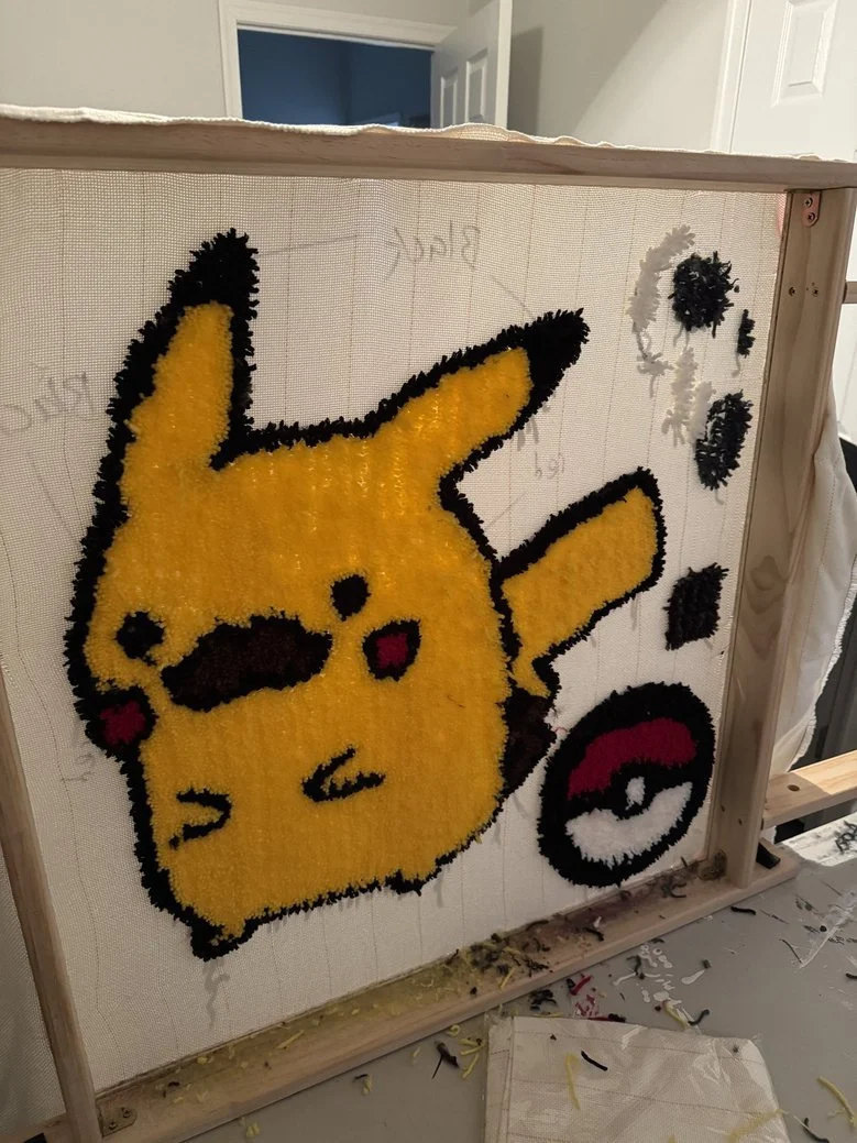 A mosaic artwork of Pikachu made with textured materials, featuring Pikachu with a pencil in its mouth, an angry expression, and a Pokéball nearby.