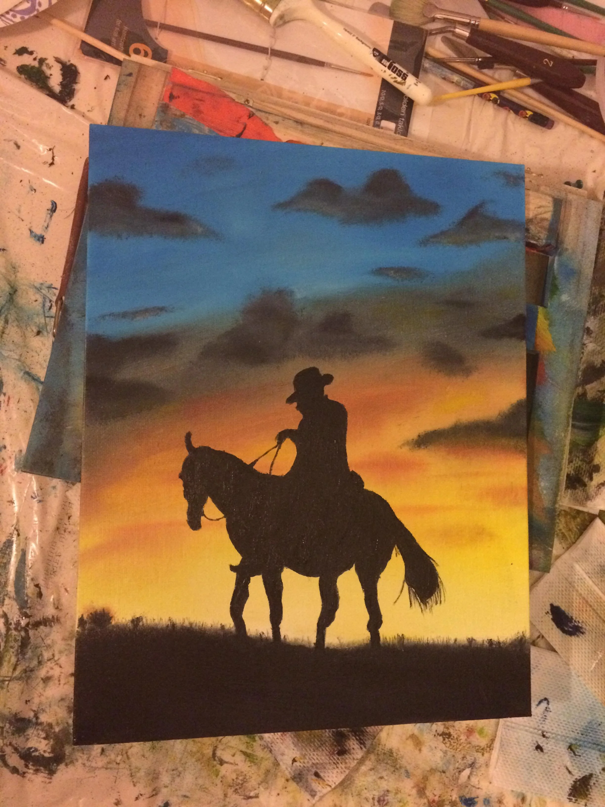 Silhouette of a person riding a horse during sunset with clouds in the sky.