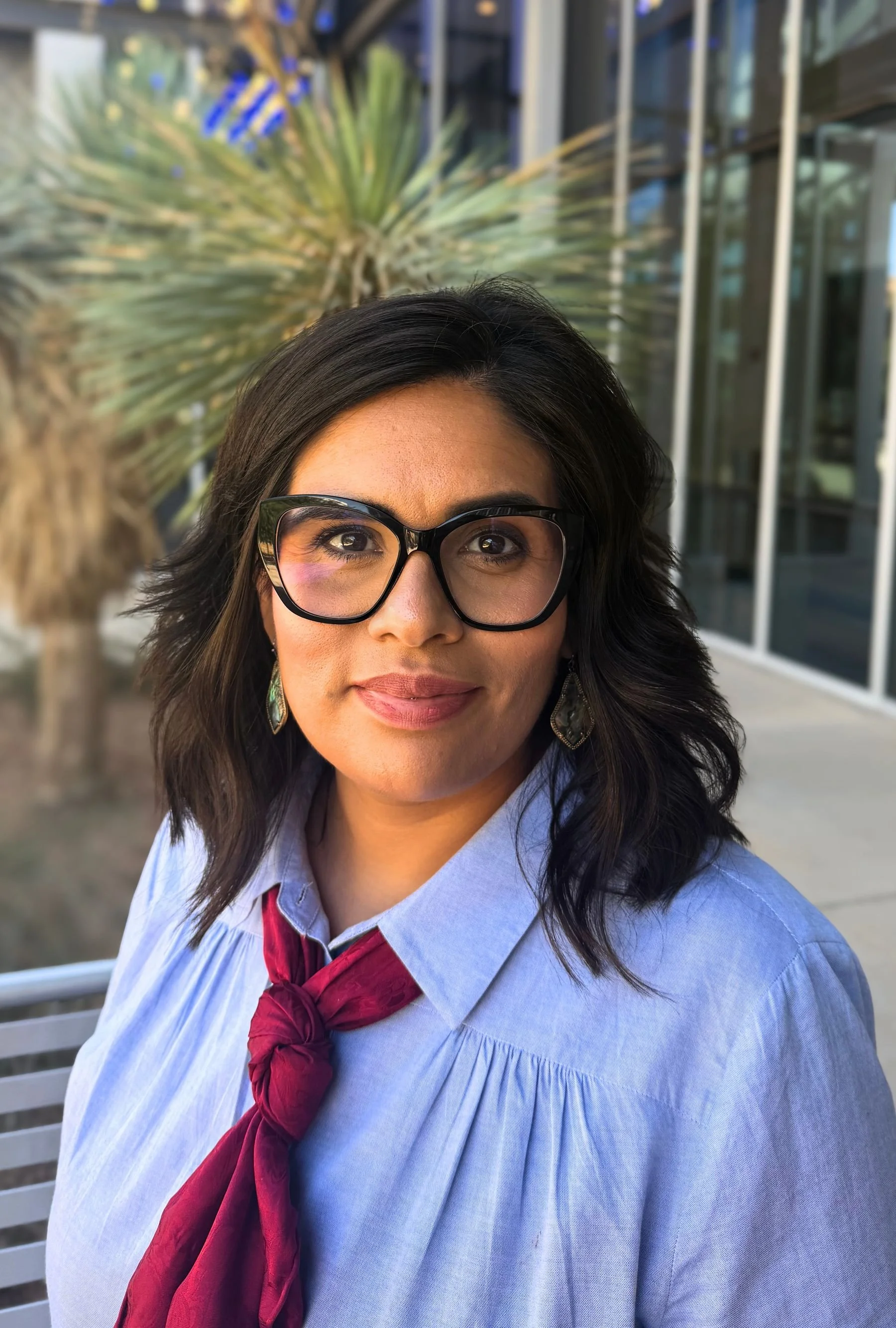 A woman with blue shirt and red tie dark hair and glasses