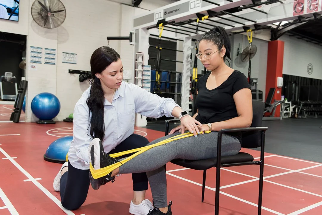 A physical therapist guides a woman in exercises with resistance bands at a fitness gym.