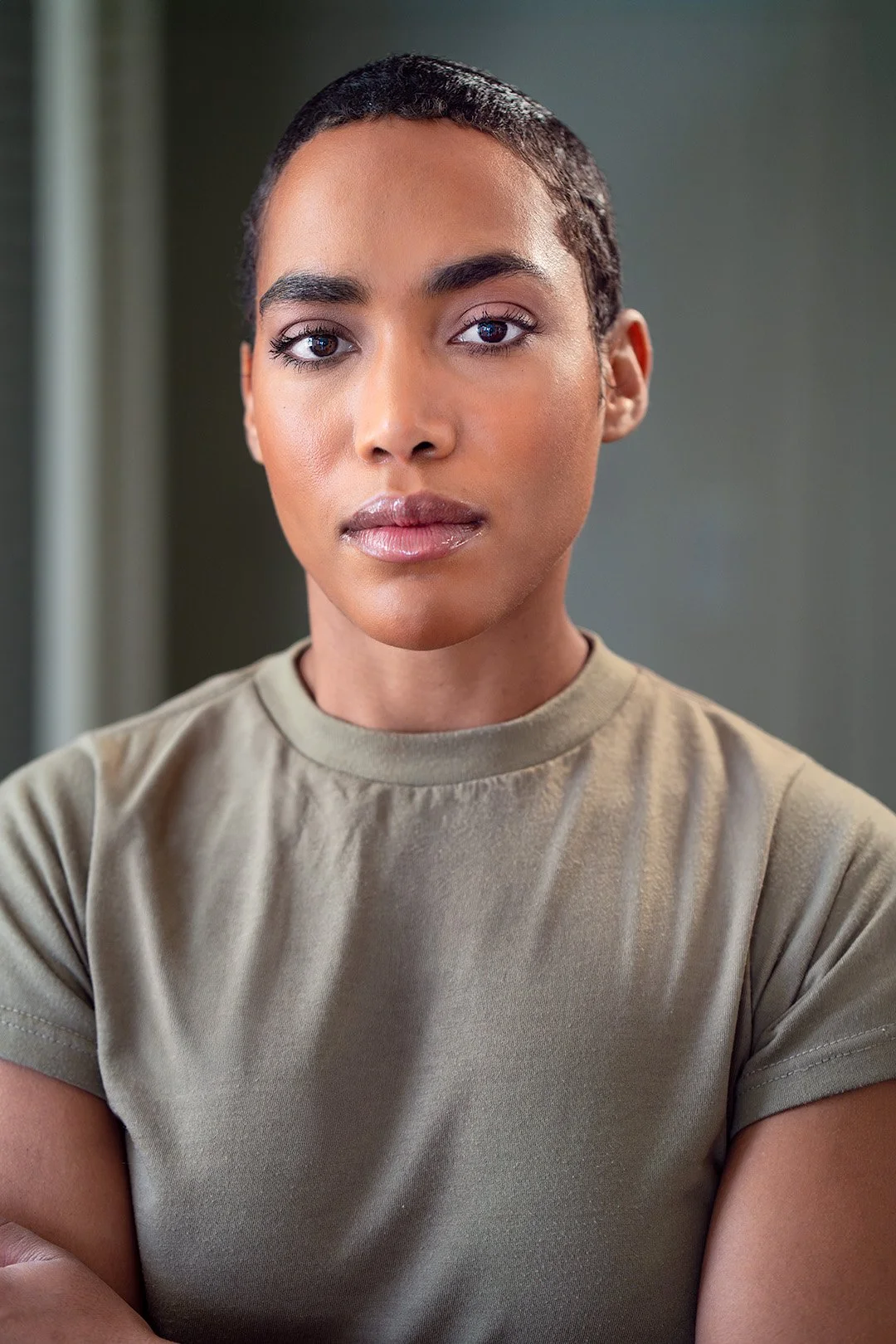 A woman with short black hair, blue eyes, and a warm expression, wearing a sleeveless rust-colored top, against a neutral background.