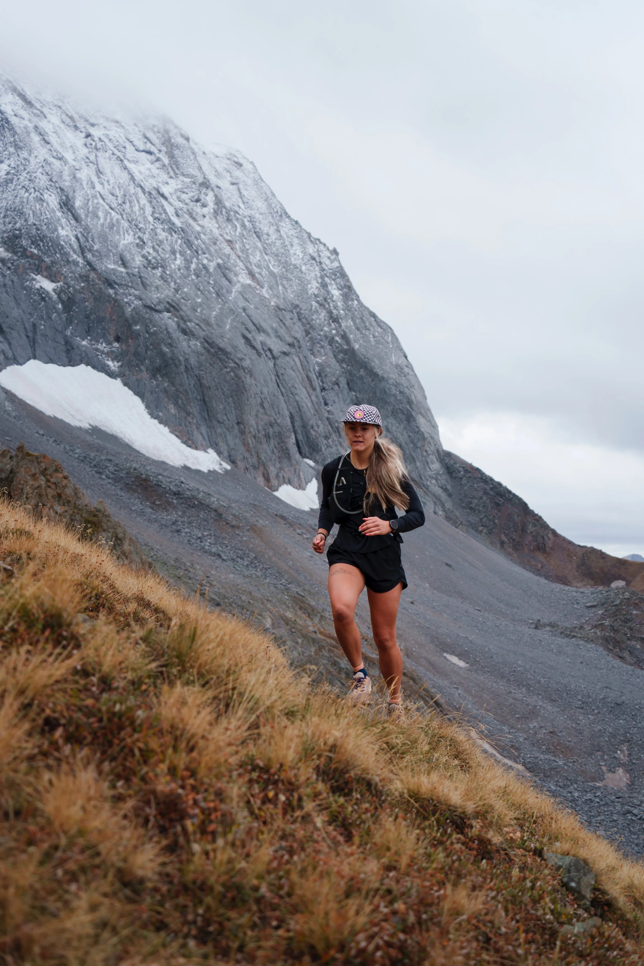 A woman trail running on a mountainous landscape with rocky terrain and patches of snow.