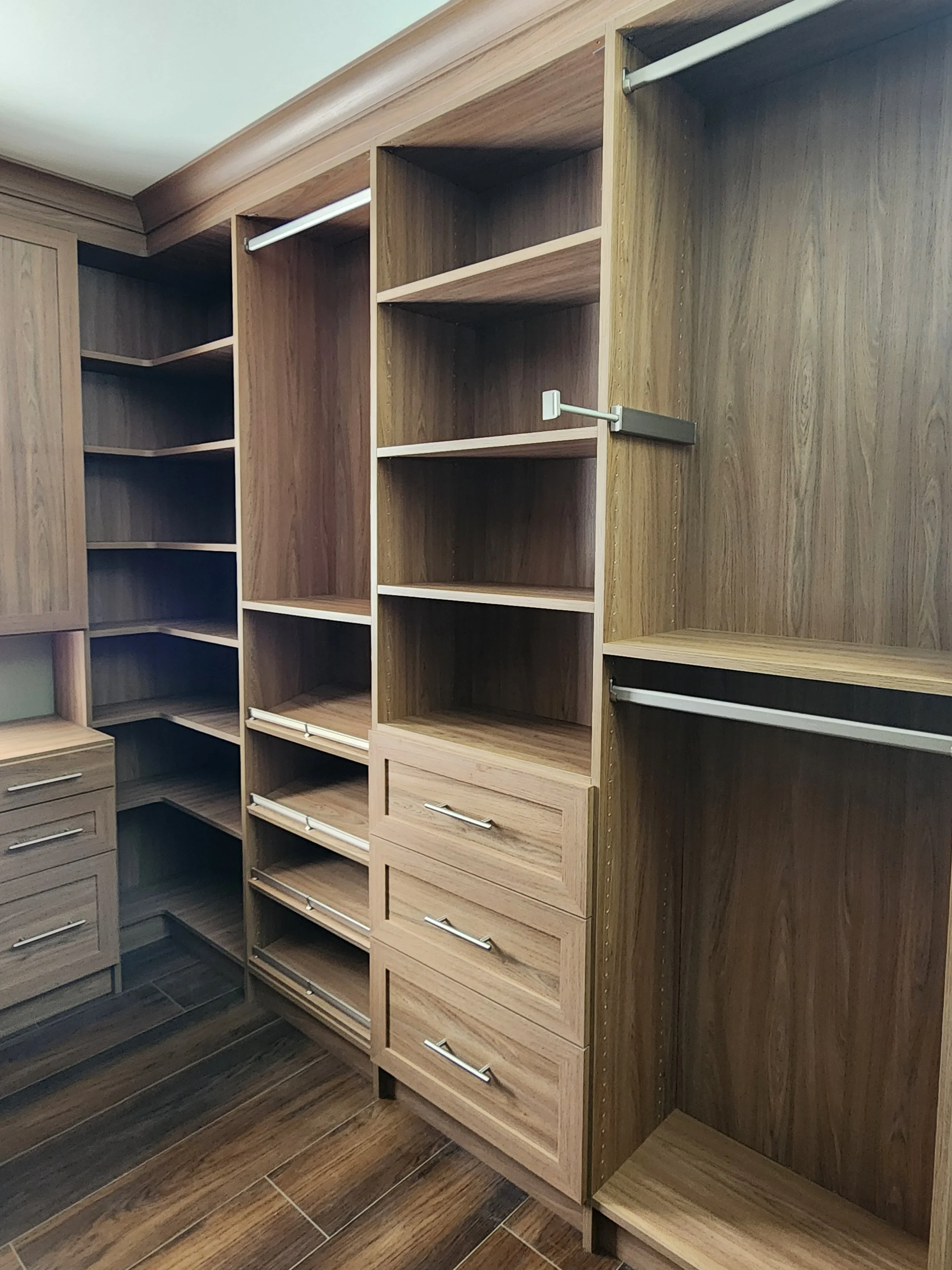 Walk in Closet in medium brown color with drawers, hanging units, slanted shoe shelves, corner unit, crown moldingand vanity