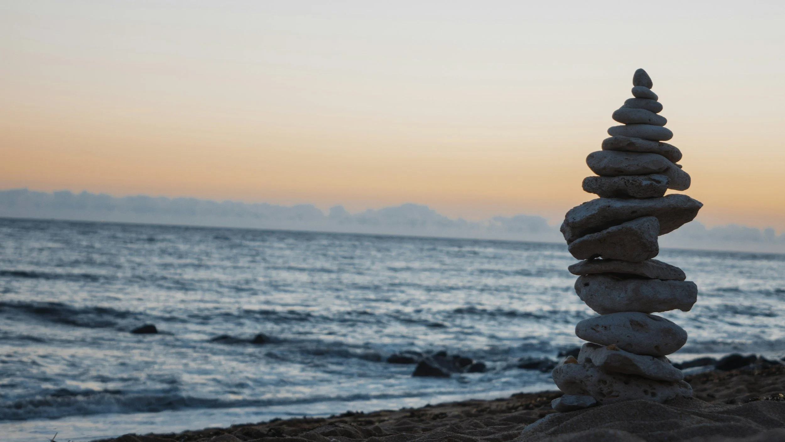 Stack of rocks on the beach during sunset with the ocean in the background.