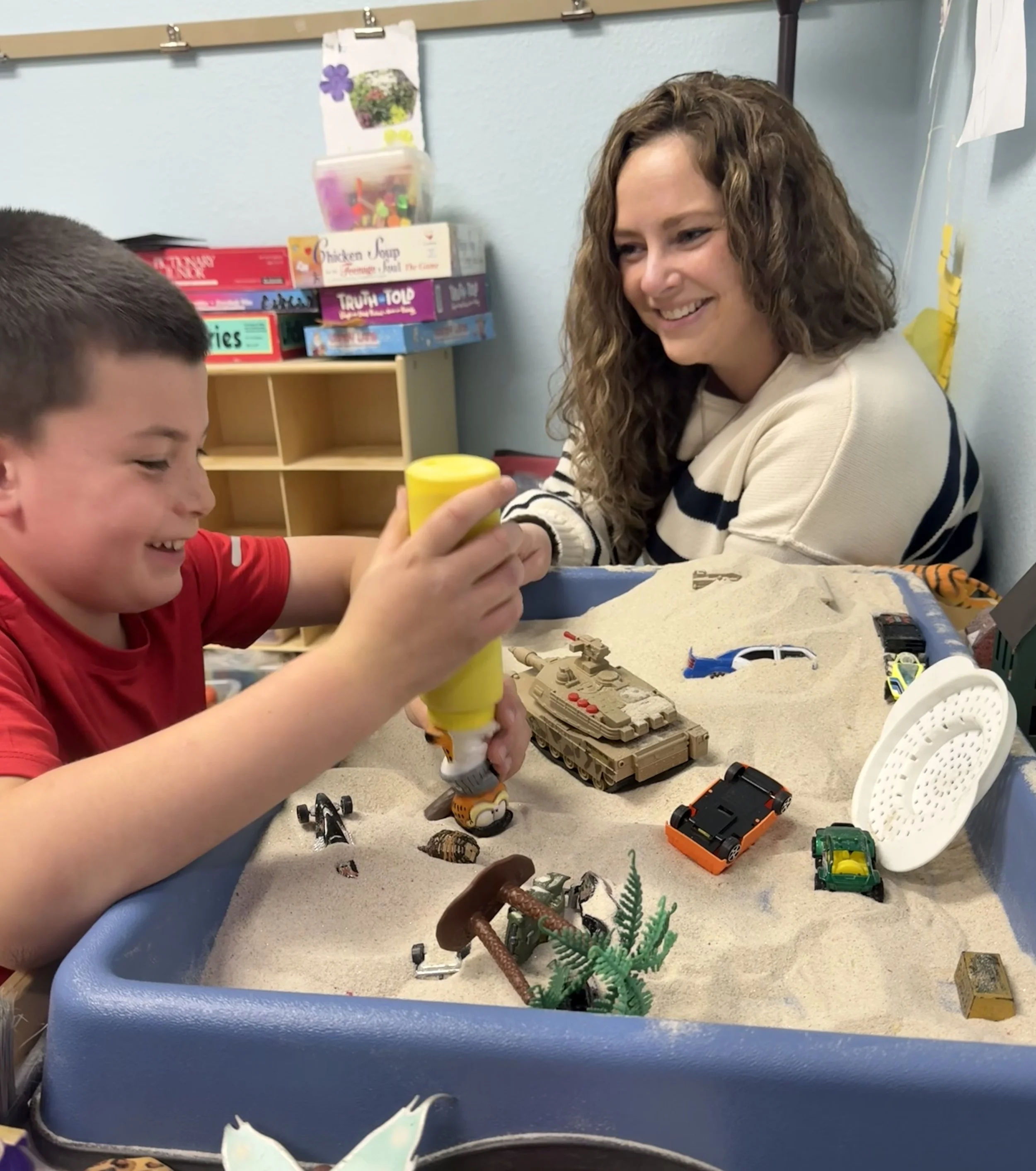 A mental health professional guides a child through a play therapy intervention using sand tray.