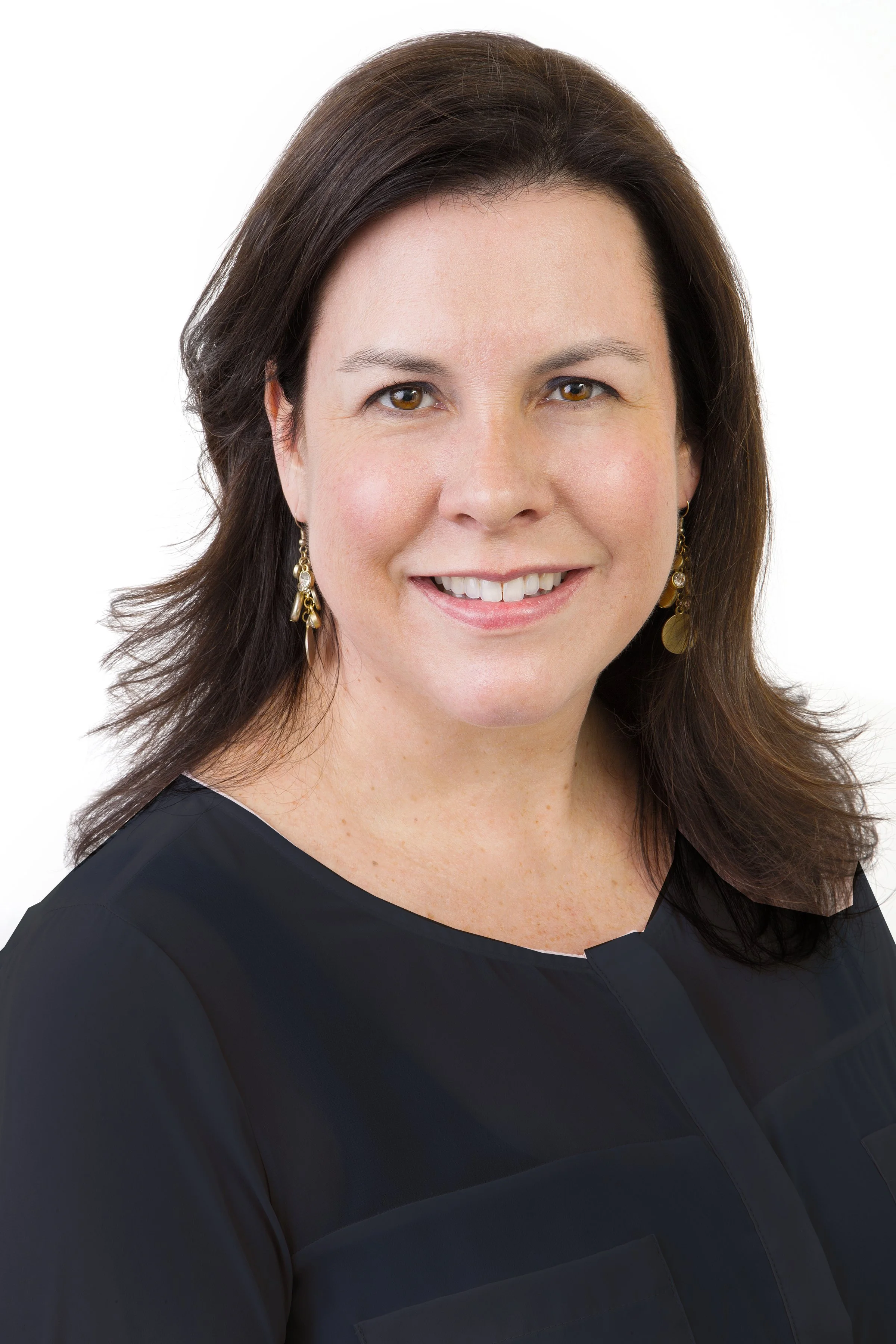 Headshot of a smiling woman with shoulder-length brown hair and earrings, wearing a black top, against a white background.
