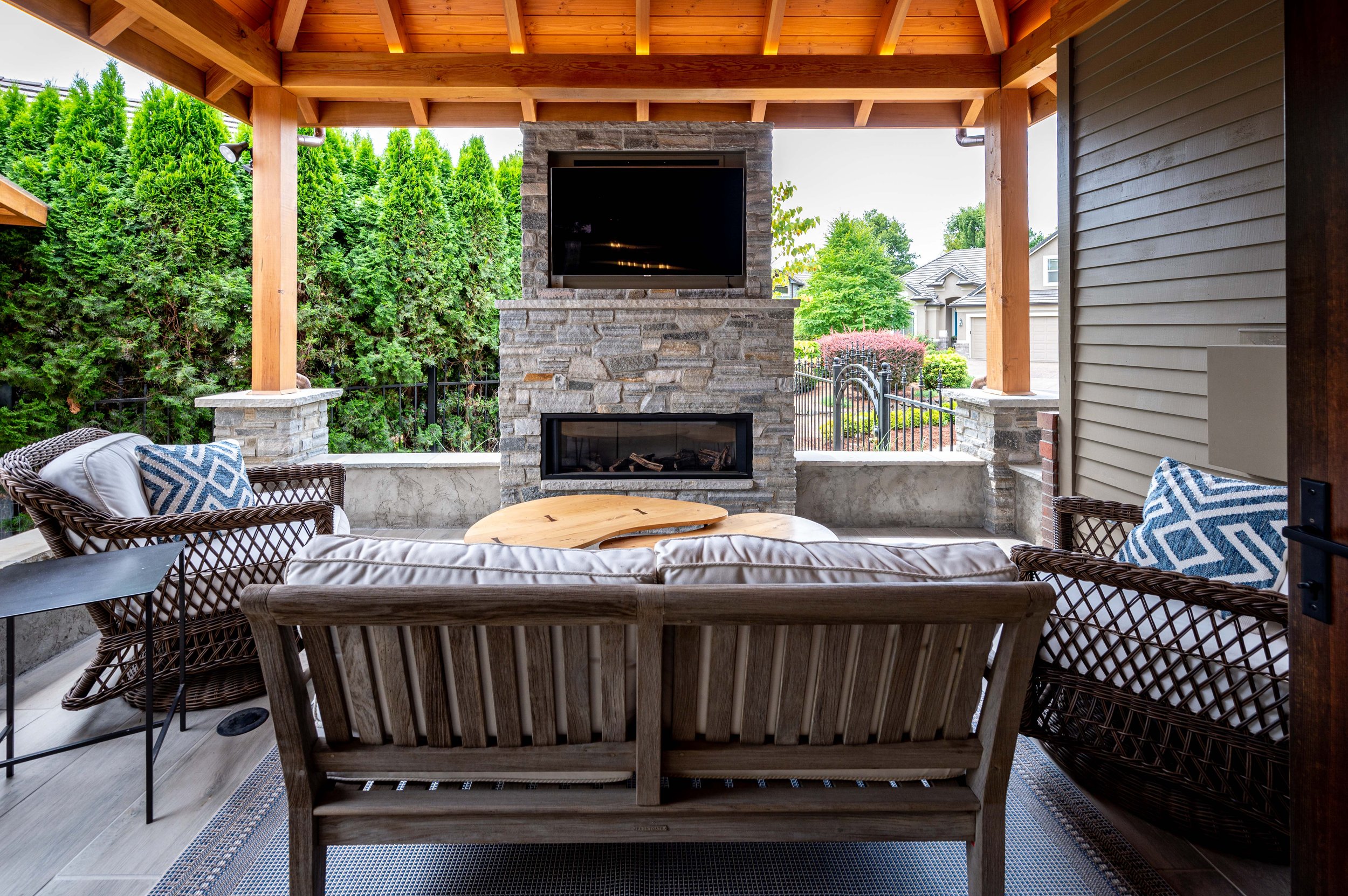 Covered outdoor seating area with stone fireplace and mounted TV