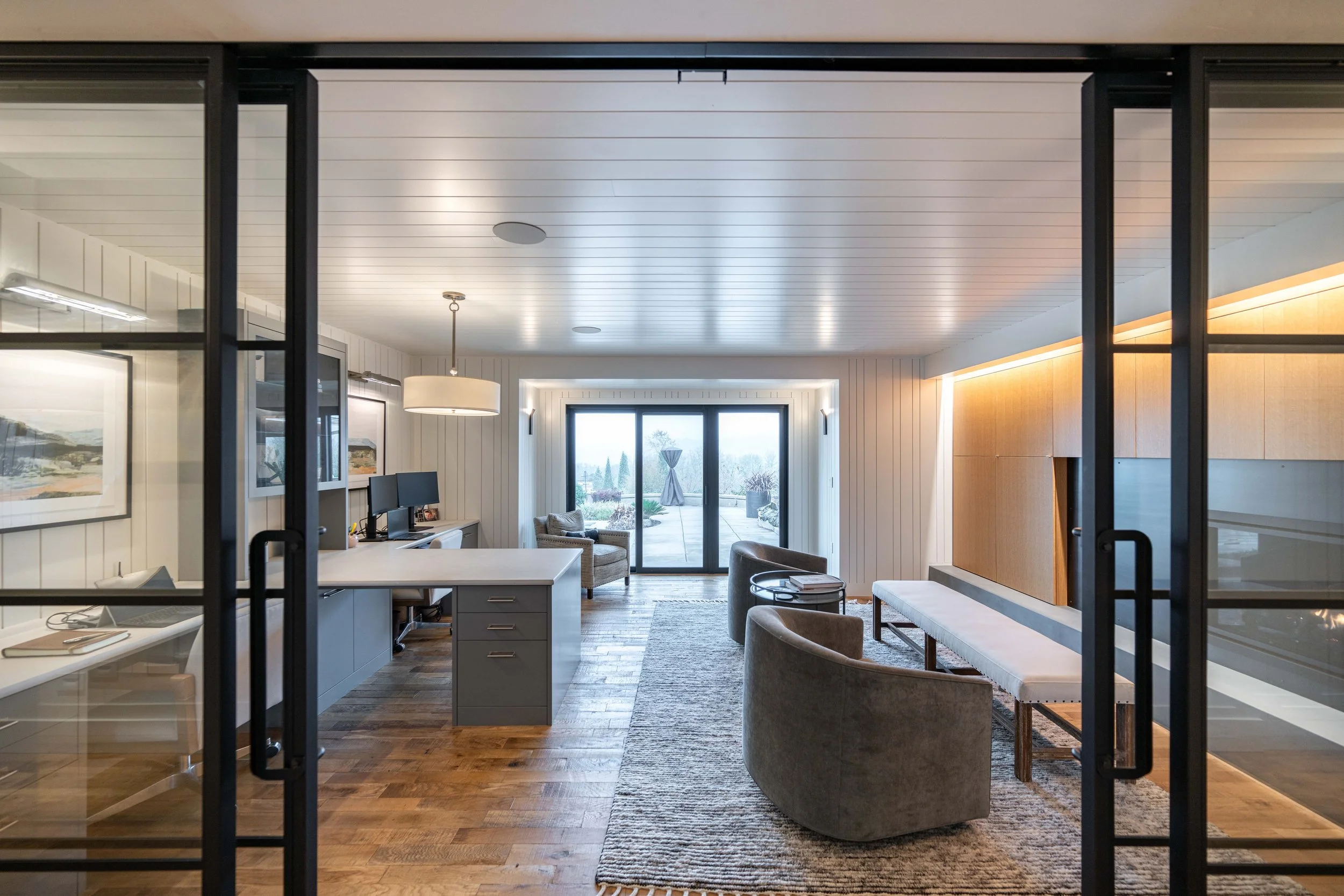Office with glass doors, wood flooring, desks, and large windows overlooking the yard