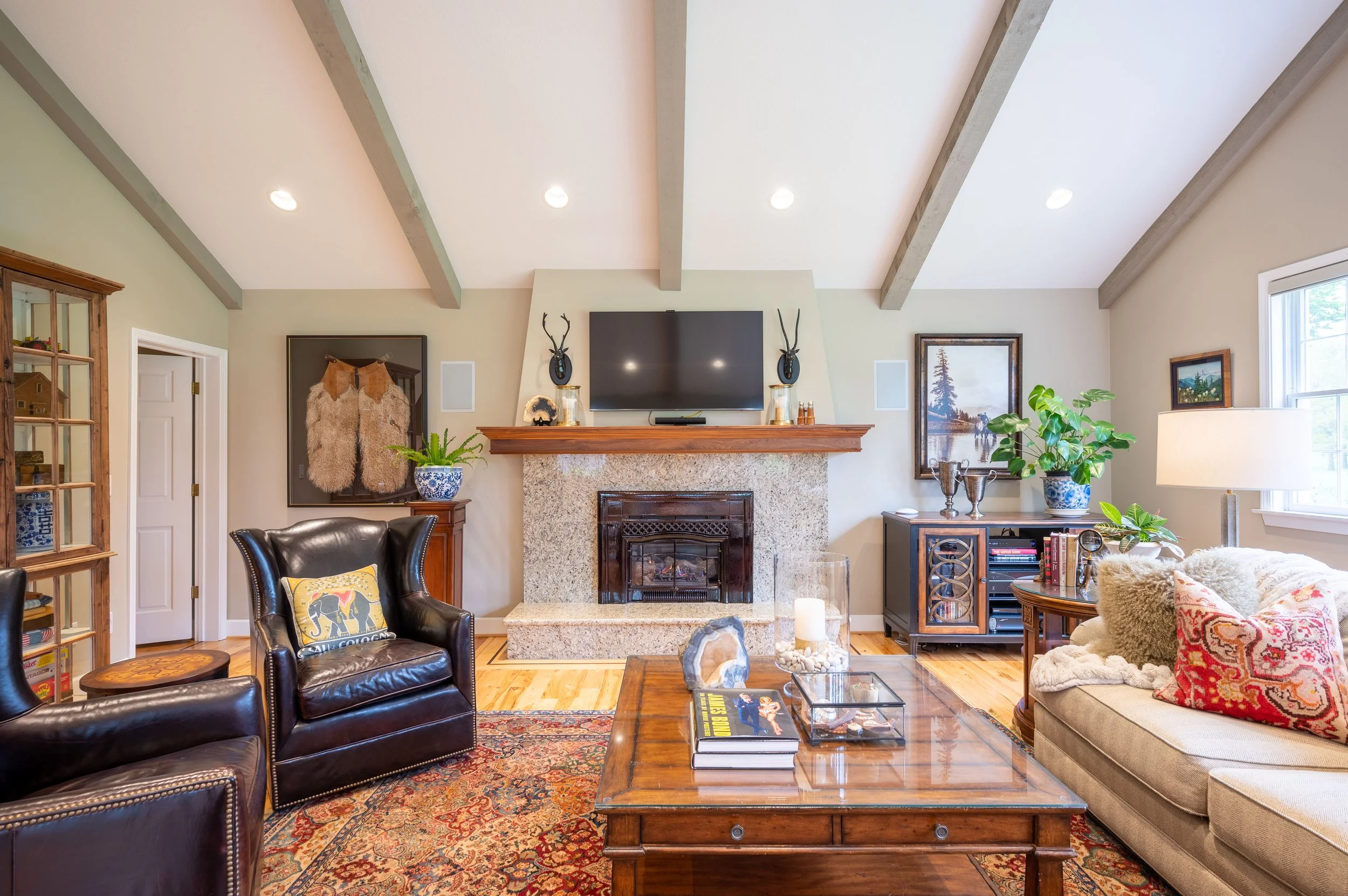 Living room with stone fireplace, wood beams, and built-in shelving