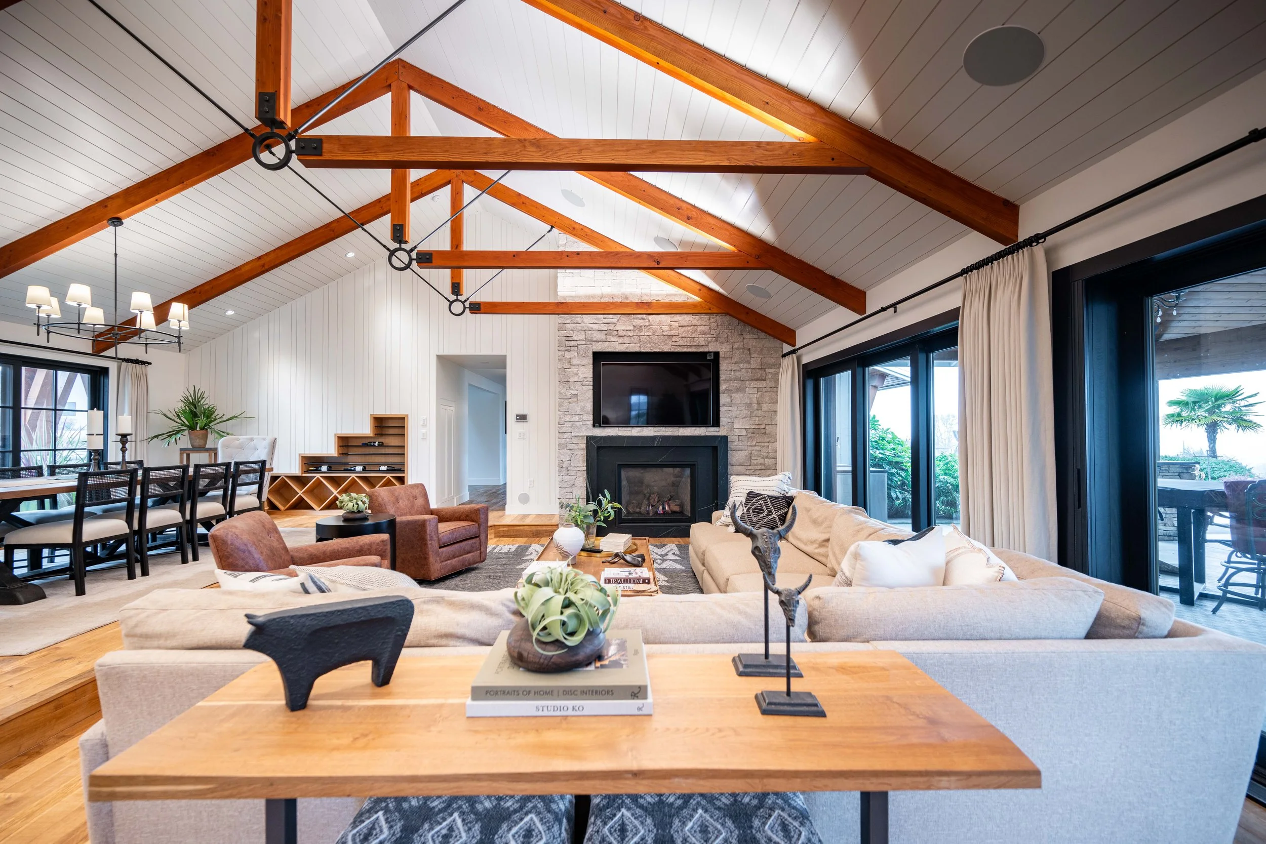 Open-concept living room with vaulted ceilings, exposed wood beams, and stone fireplace