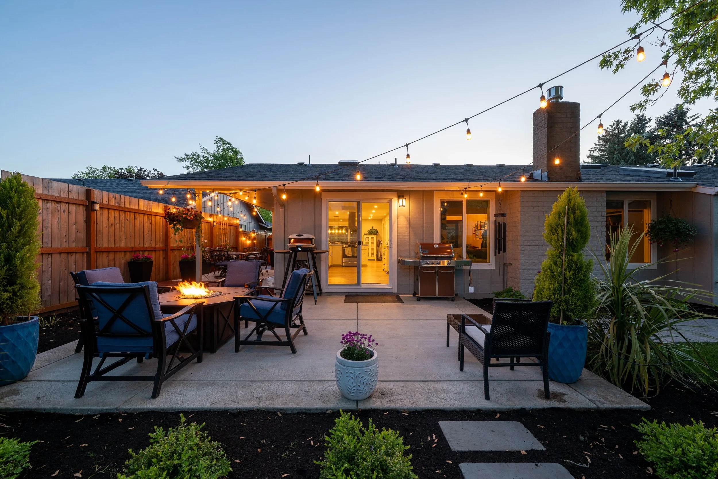 Outdoor patio with seating, string lights, and illuminated home exterior at dusk