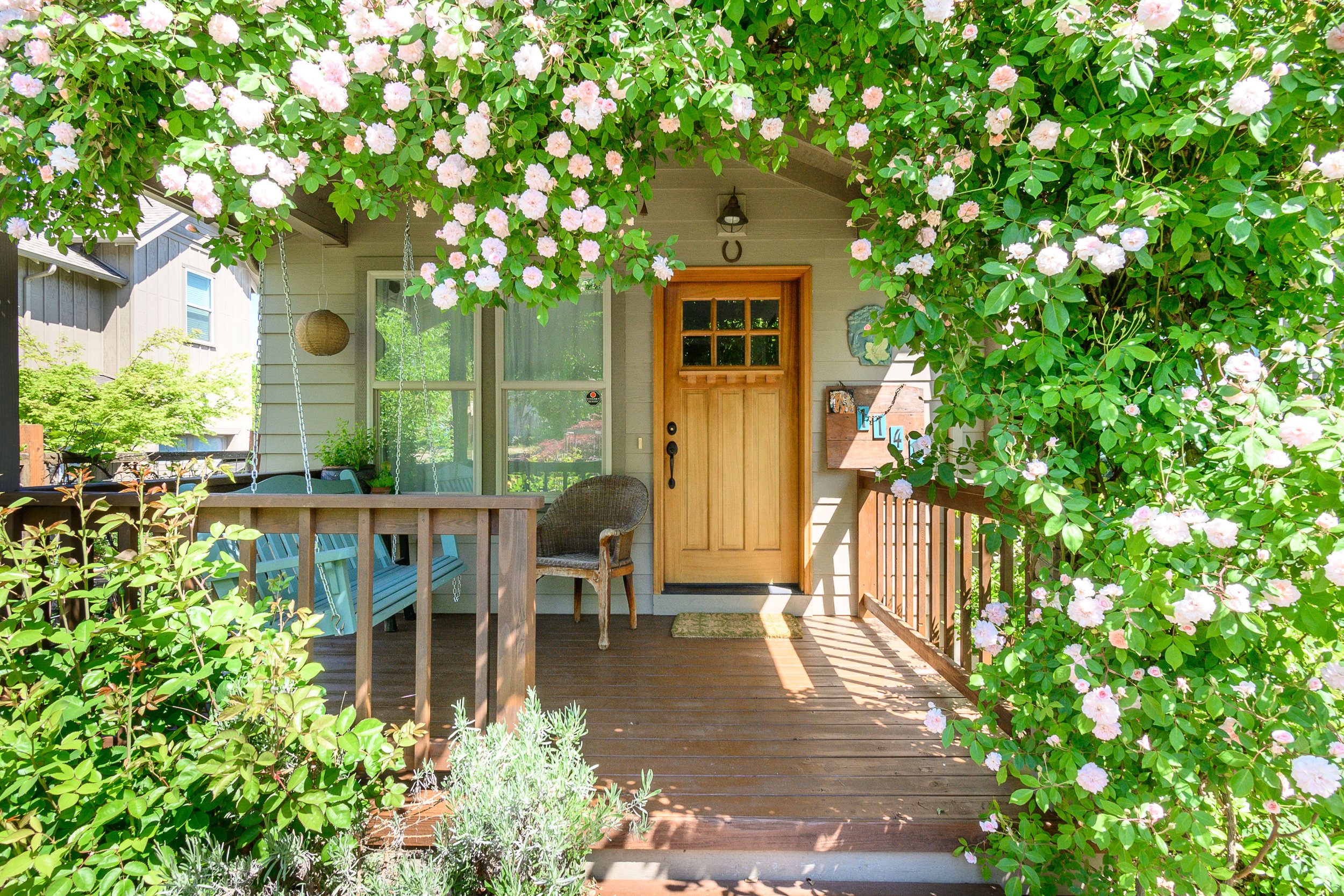 Charming bungalow front porch framed by climbing roses and lush garden greenery