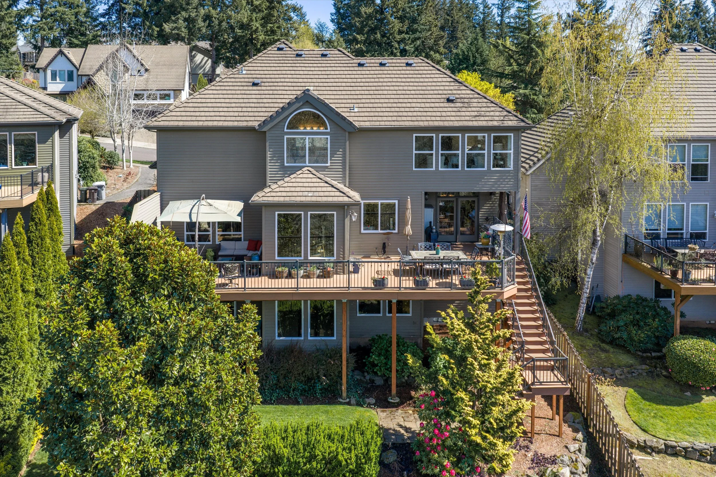 Drone exterior photo of the back of a home featuring a deck and mature landscaping