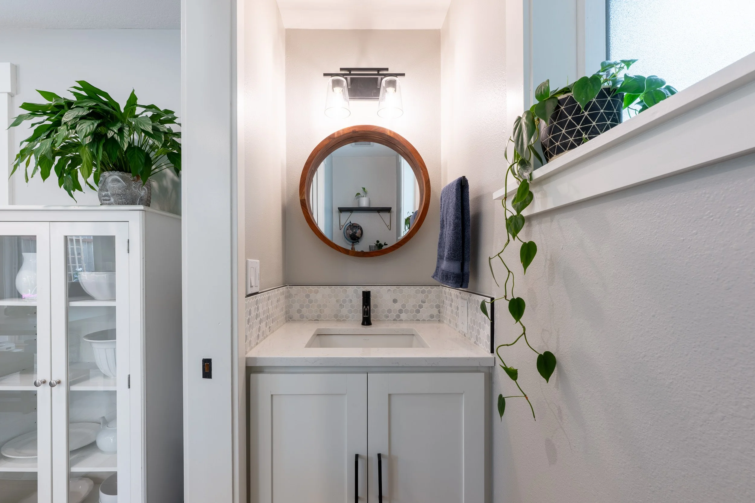 Bathroom vanity with round mirror, marble countertop, and wall-mounted faucet