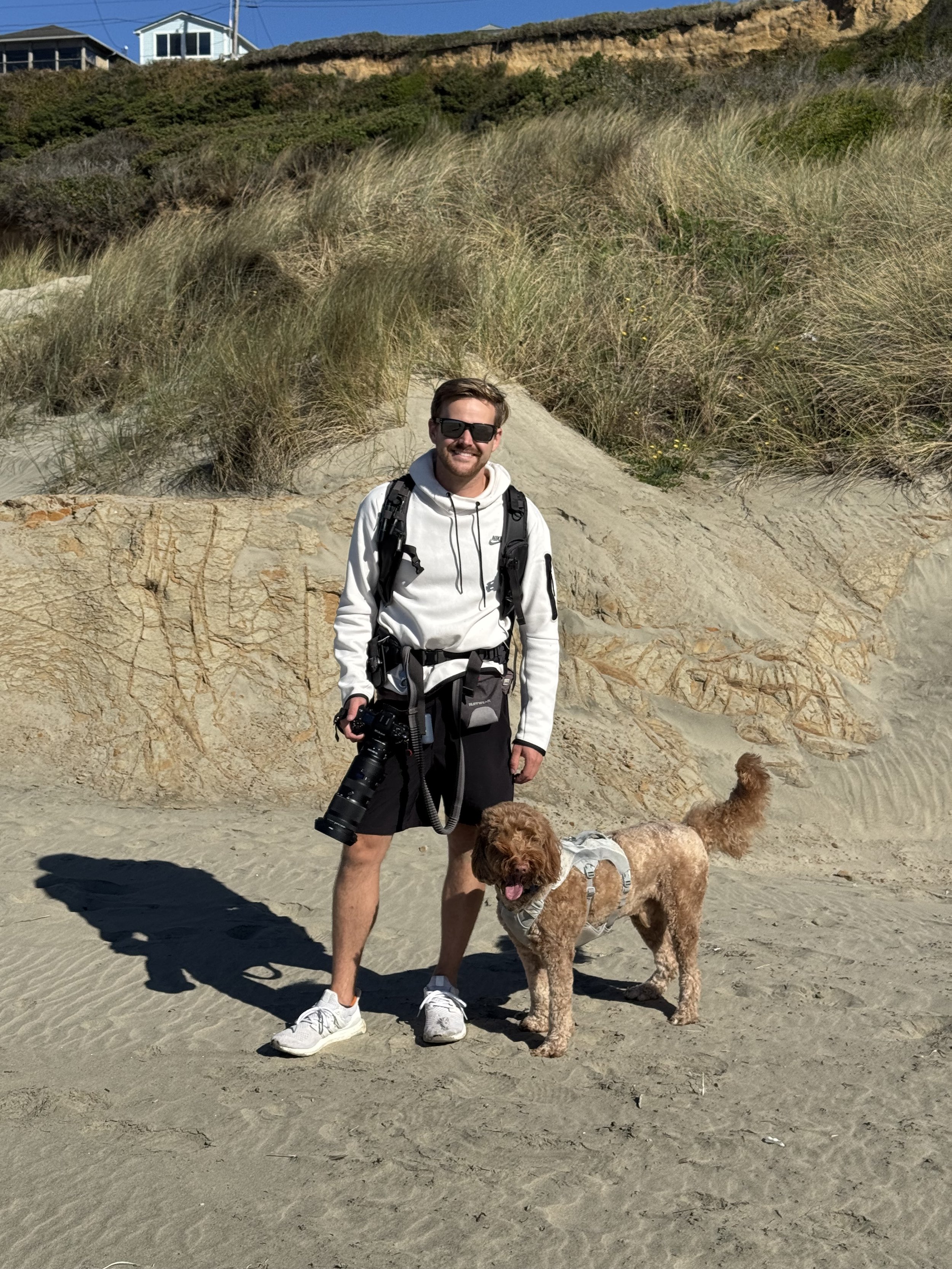 Alex Maclean, media director and real estate photographer, standing on the Oregon coast with his camera and dog