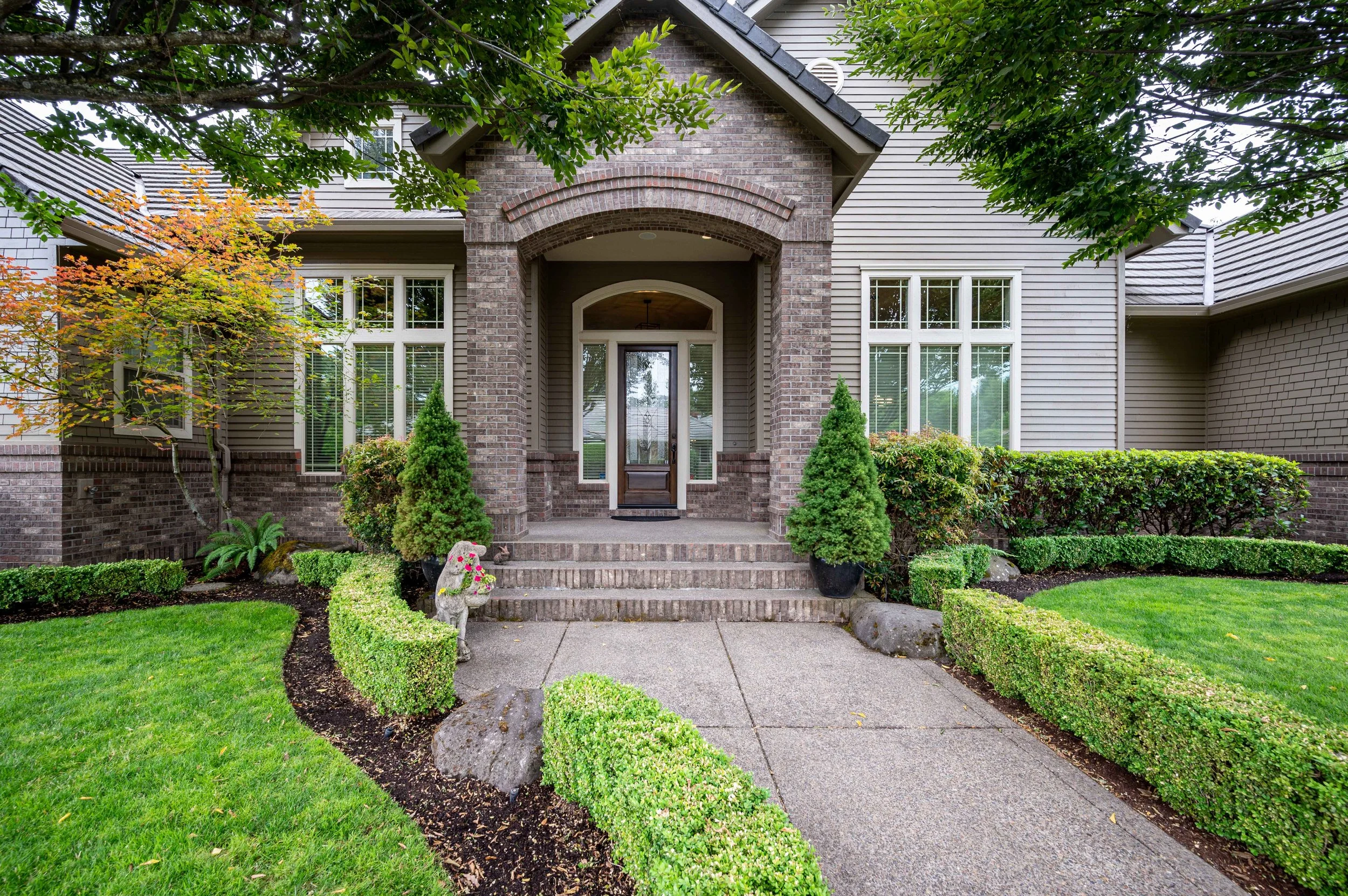 Front entry of craftsman-style home with brick archway, landscaping, and walkway