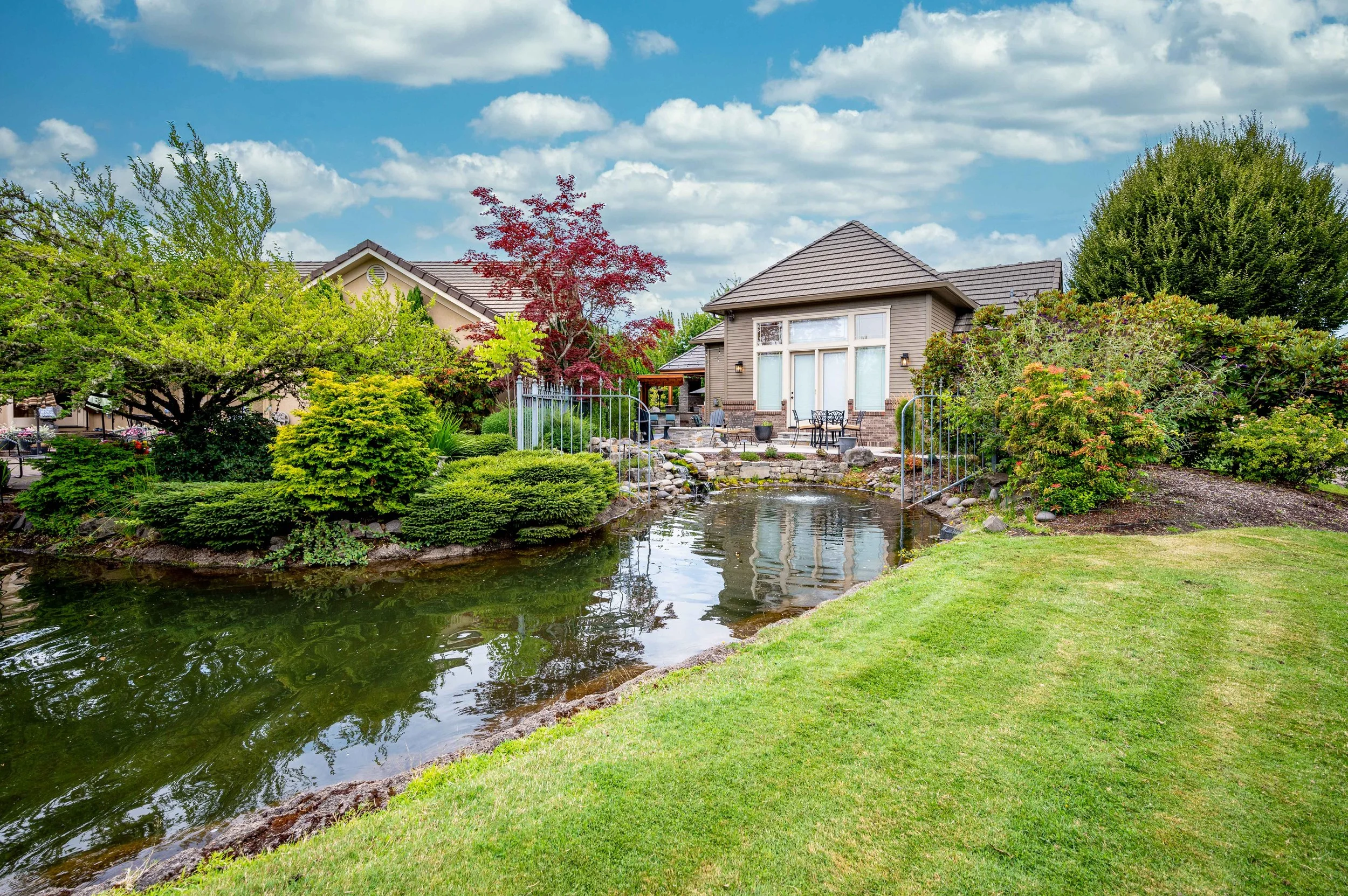 Backyard view with landscaped pond, lawn, and neighboring homes under blue sky