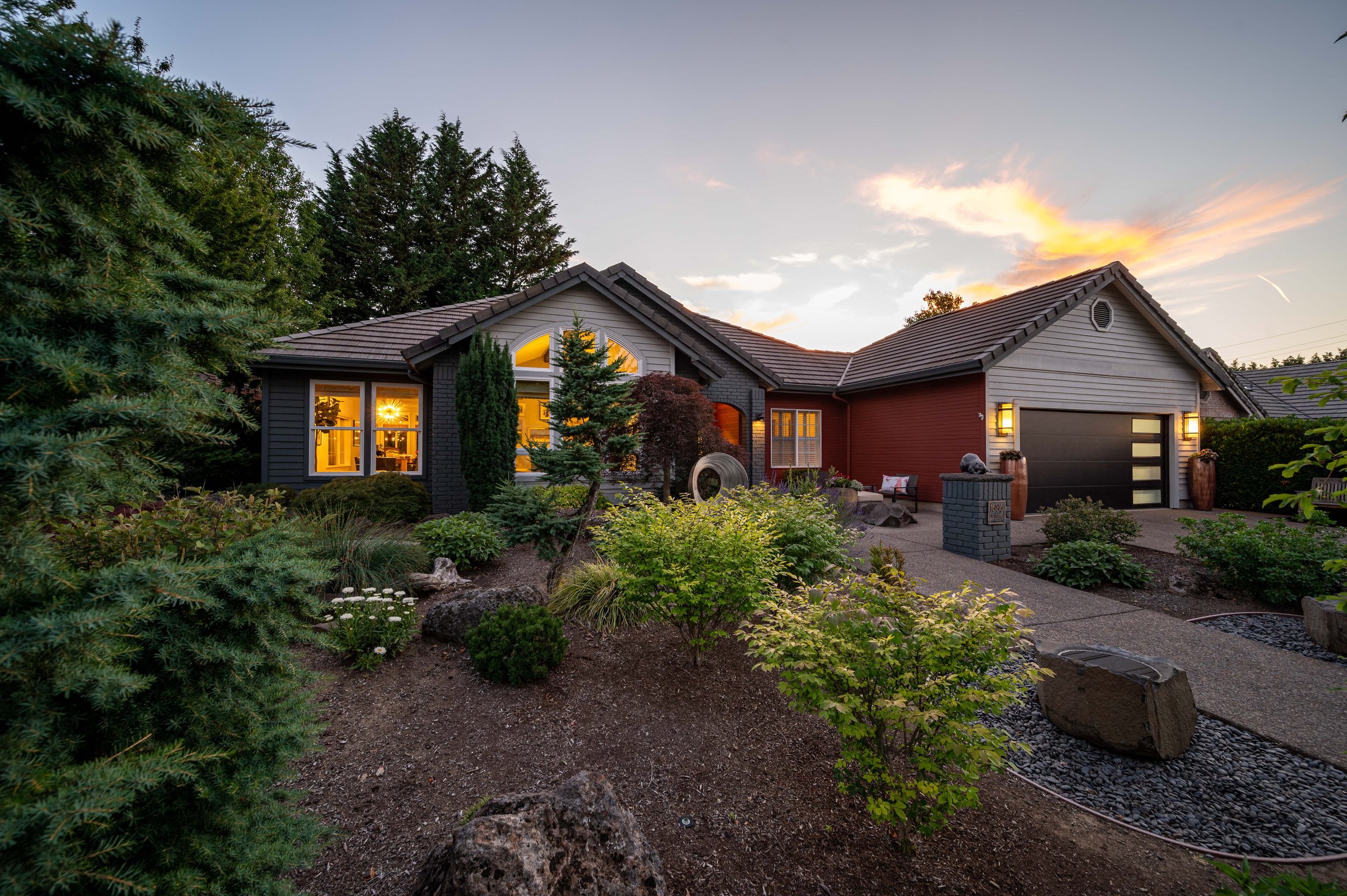 Single-story home exterior at dusk with landscaped front yard and warm interior lights