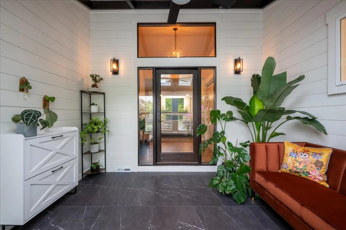 Modern entryway with black tile flooring, glass double doors, indoor plants, and warm wall sconces.