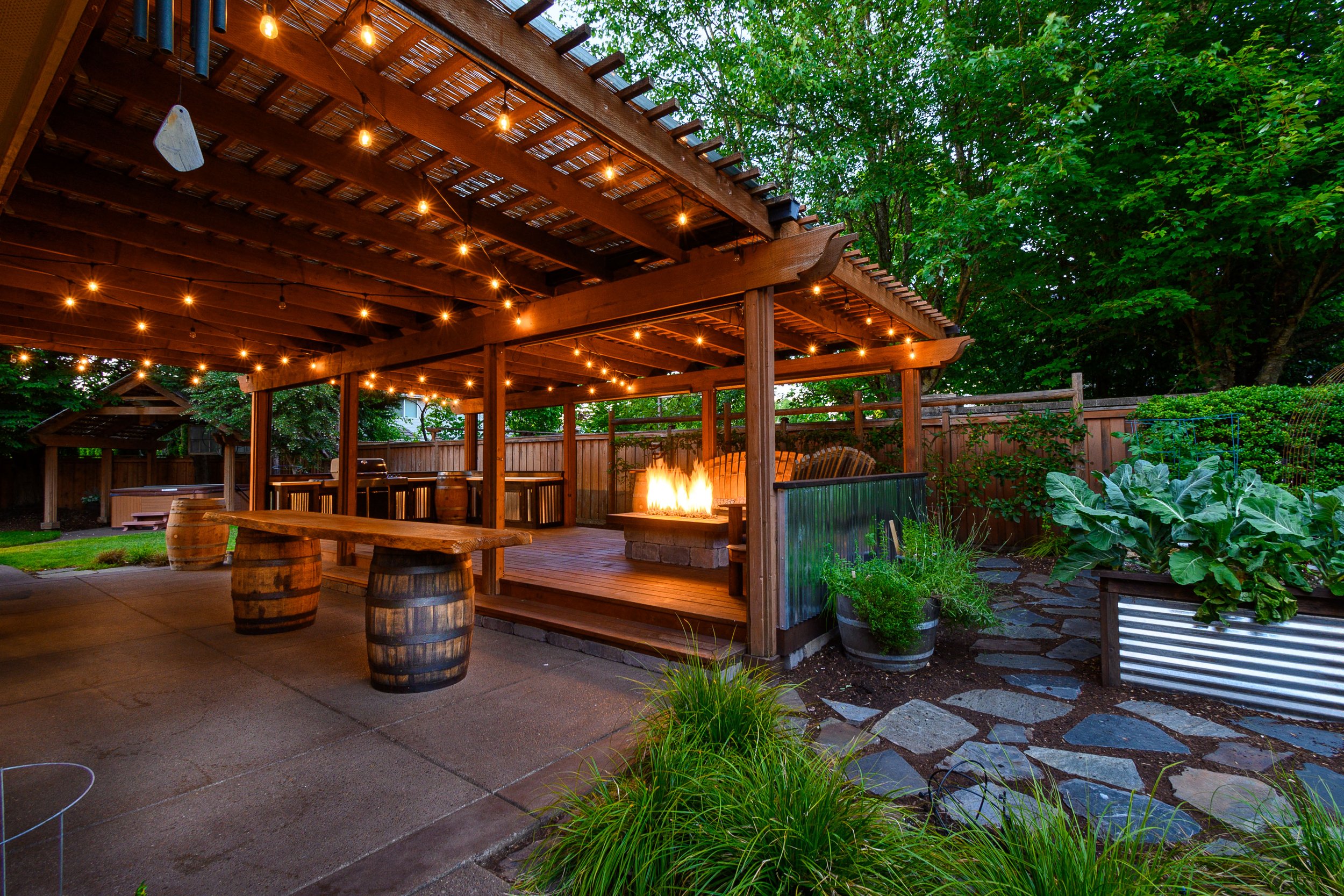 Twilight photo of a backyard with a custom deck, fire pit, string lights, and raised garden beds