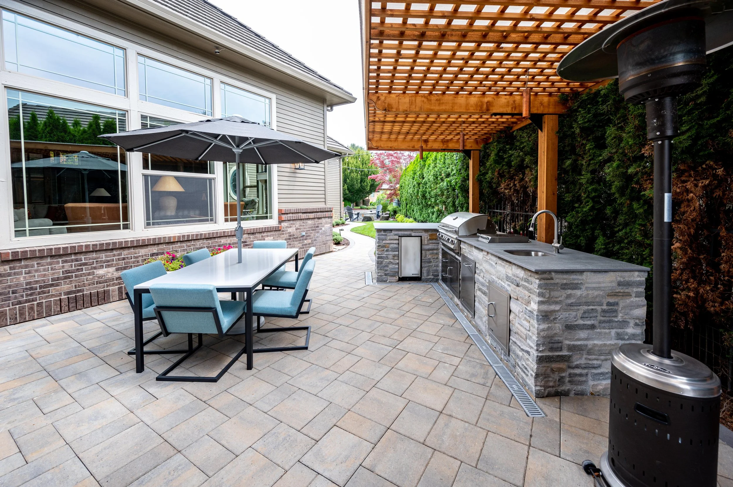Covered outdoor kitchen and patio with stone counters, pergola, and dining area