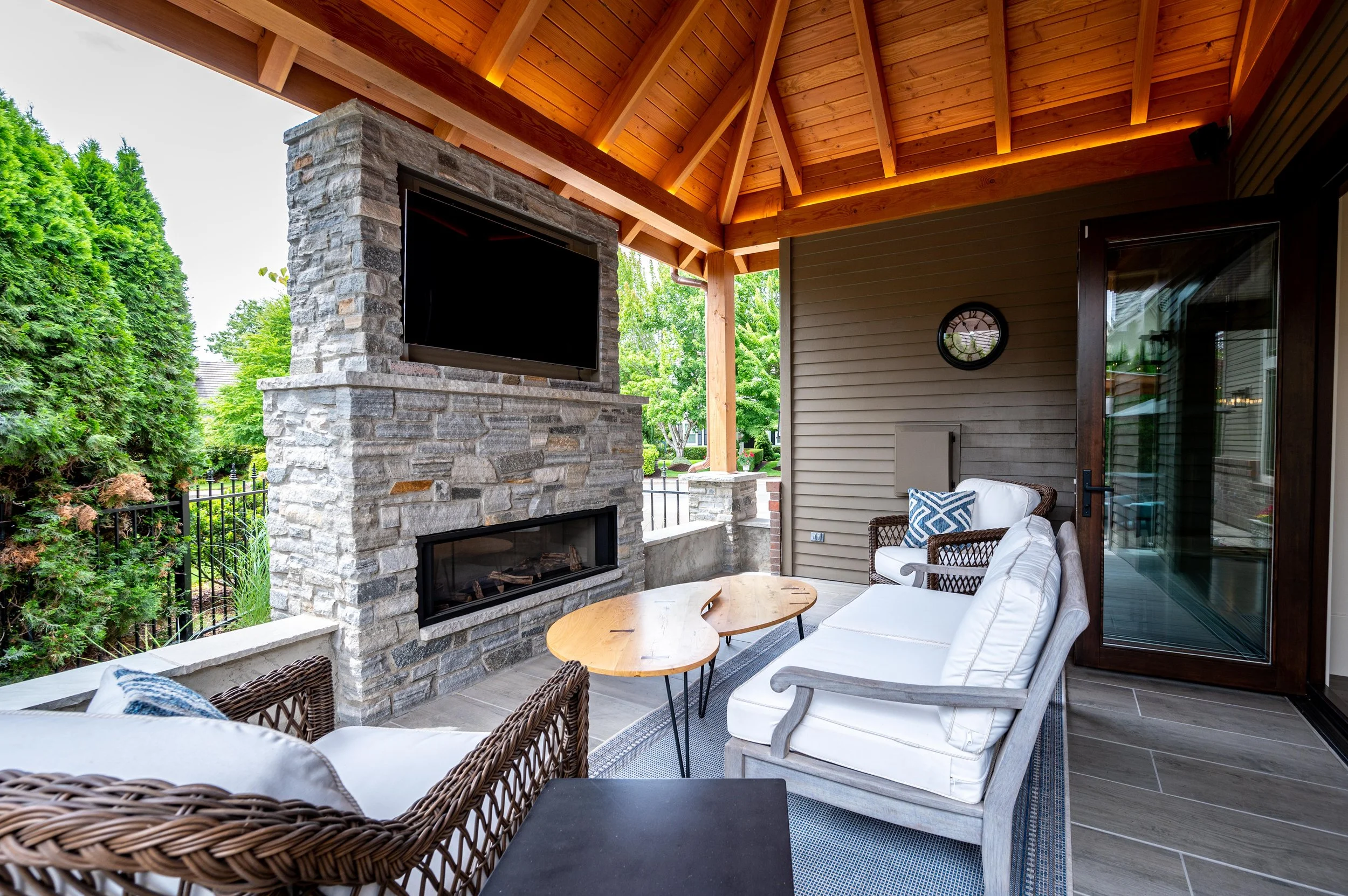 Covered outdoor living space with stone fireplace, TV, seating, and wood ceiling