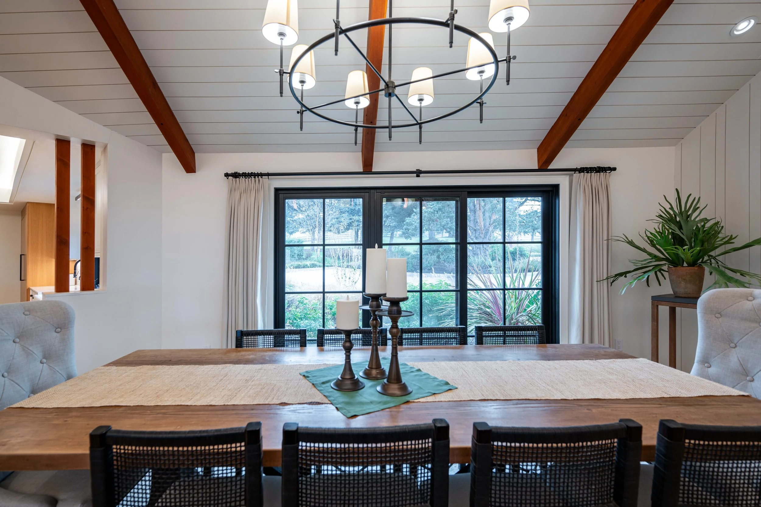 Dining area with wood table, exposed beams, and large windows overlooking the yard