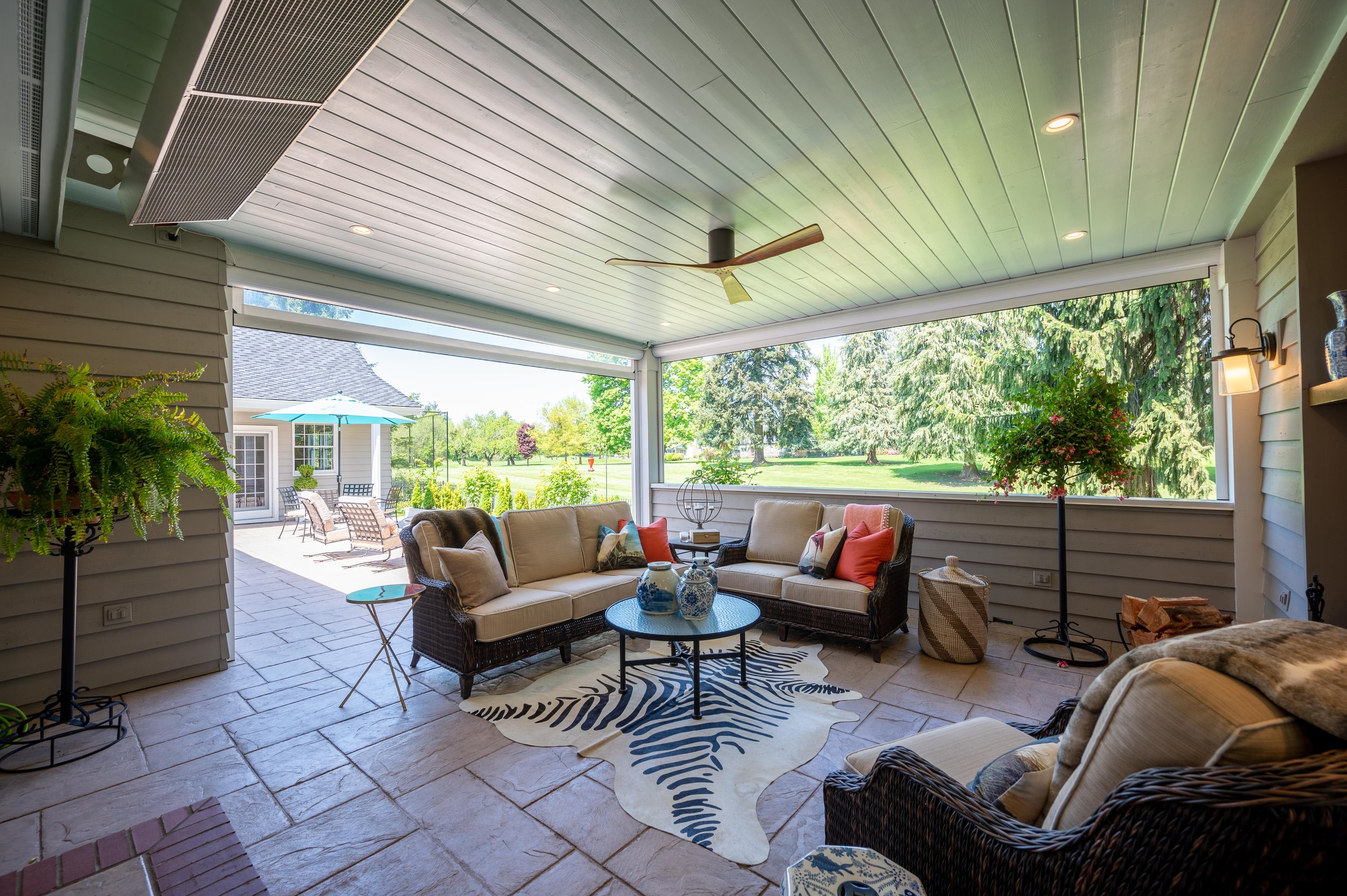 Covered outdoor patio with wicker seating, ceiling fan, and view of landscaped yard