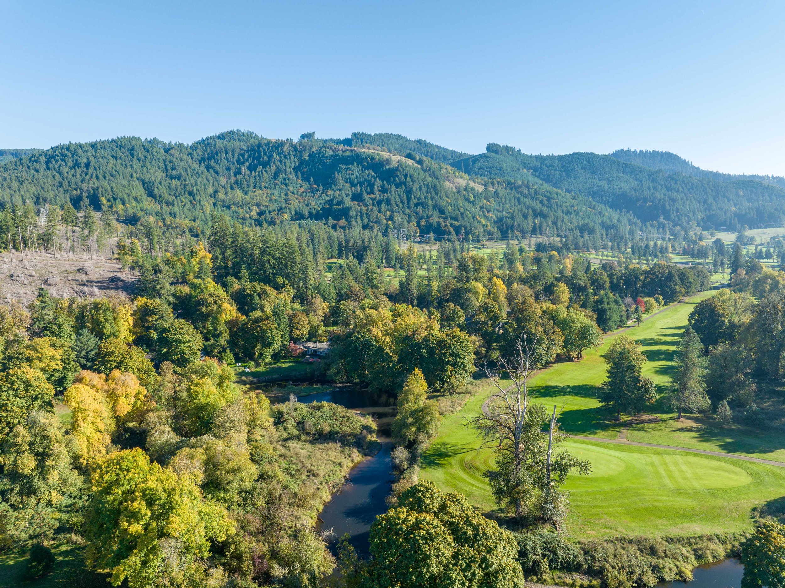 Drone photo of a home in a forested setting near a river surrounded by rolling hills
