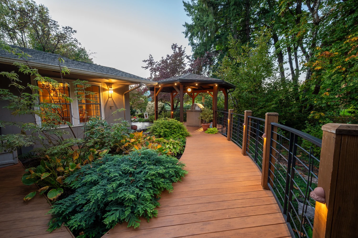 Aerial view of a riverfront home at dusk with illuminated outdoor patio, surrounded by lush trees and greenery