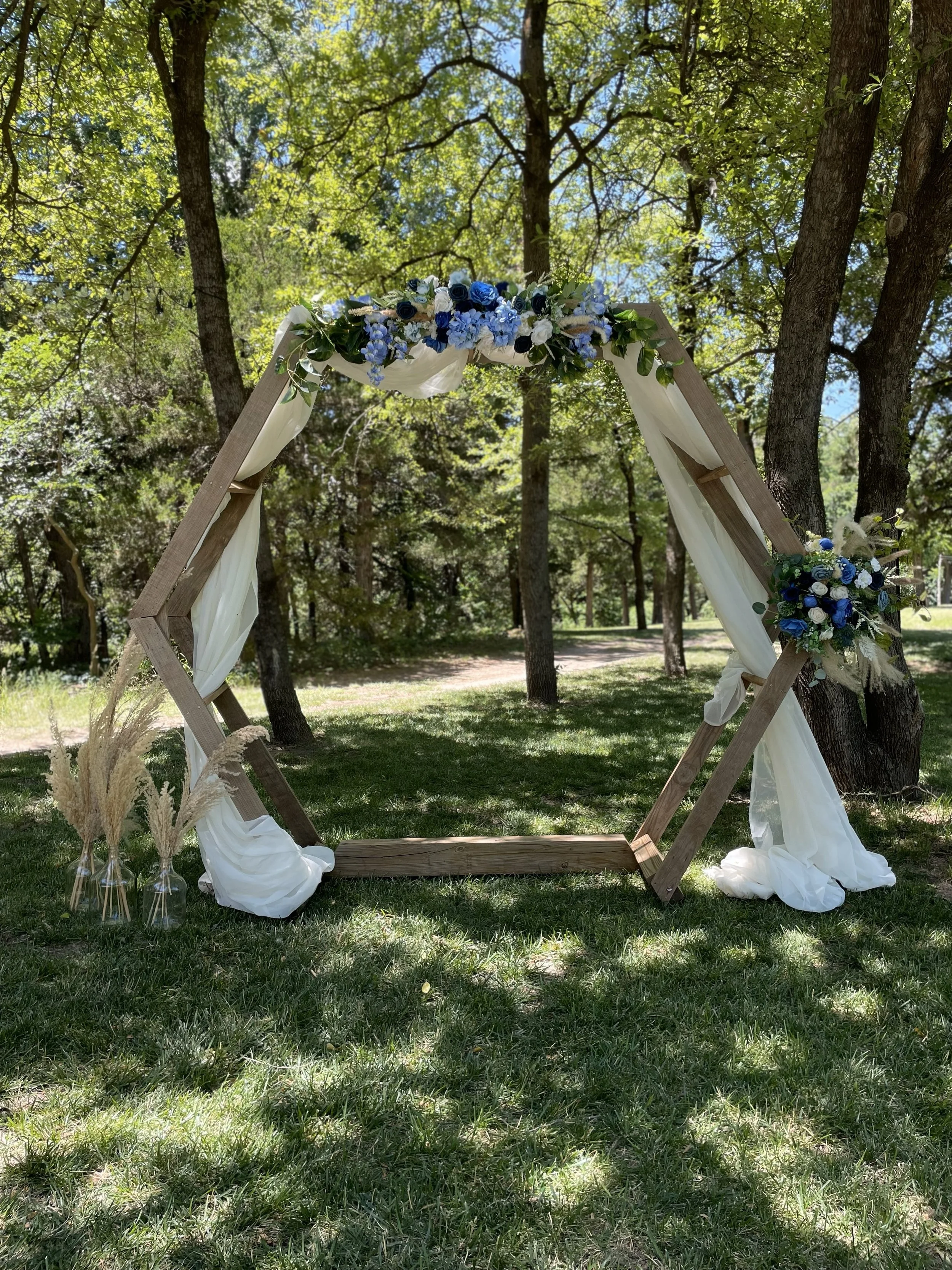 Hexagon arch with chiffon draping, blue and white flowers and pampas grass jugs, outdoor wedding, The Ranch at Woodward, Northwest Oklahoma. Barn indoor/outdoor wedding venue