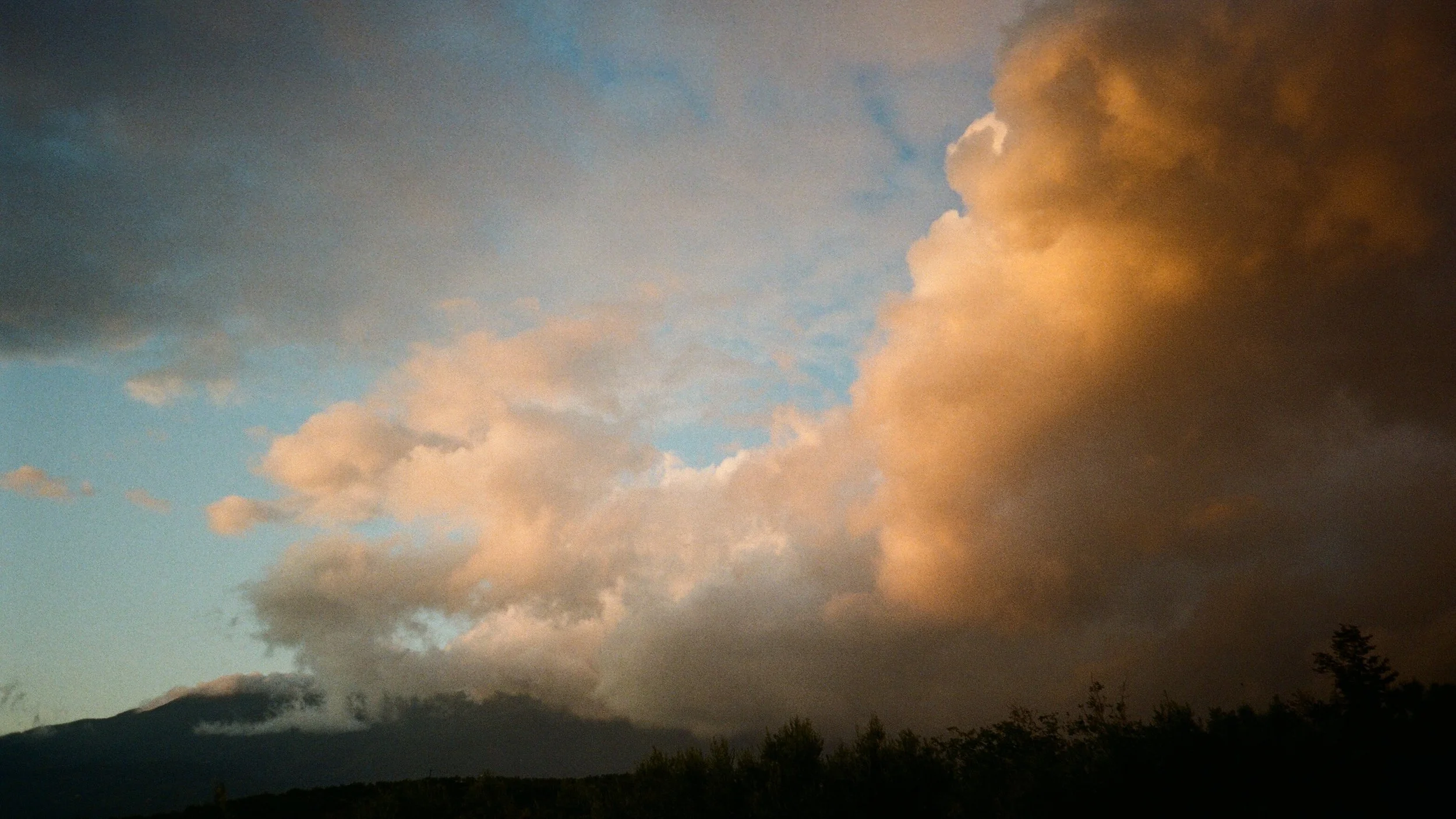 Cloudy sky with orange and dark gray clouds over a mountain landscape.