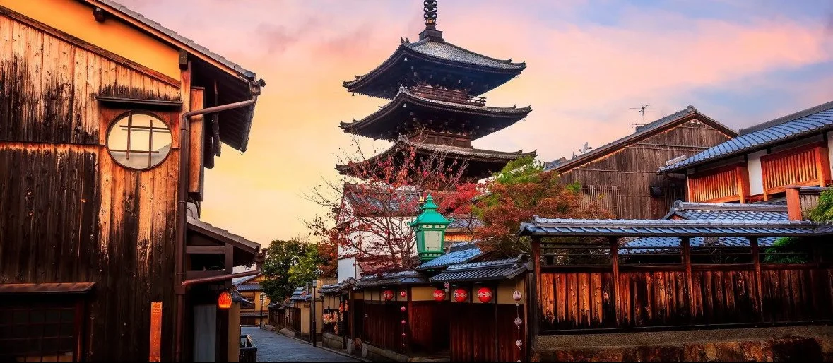 Traditional Japanese street with wooden buildings and a pagoda in the background during sunset.