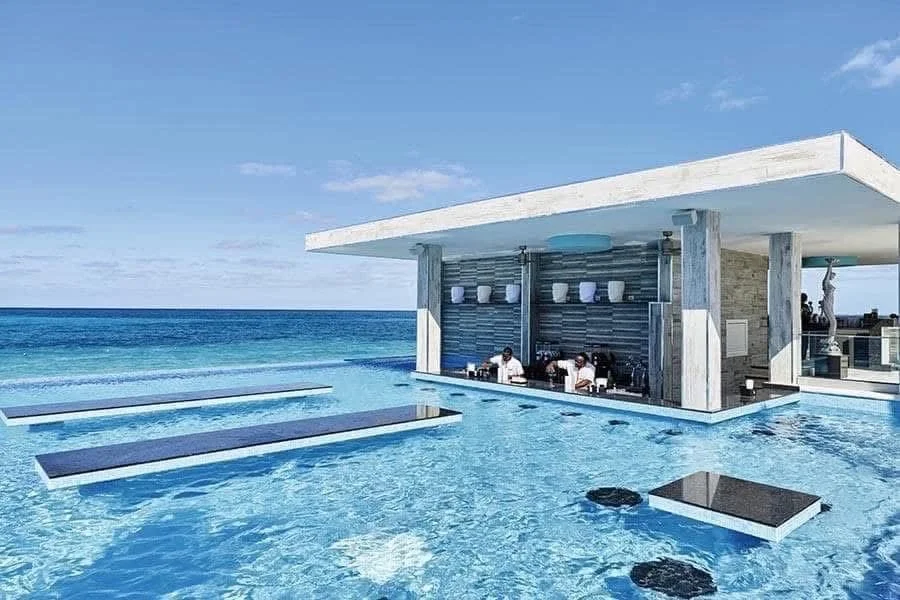 Luxury infinity pool overlooking the ocean with a modern poolside bar area and blue sky.