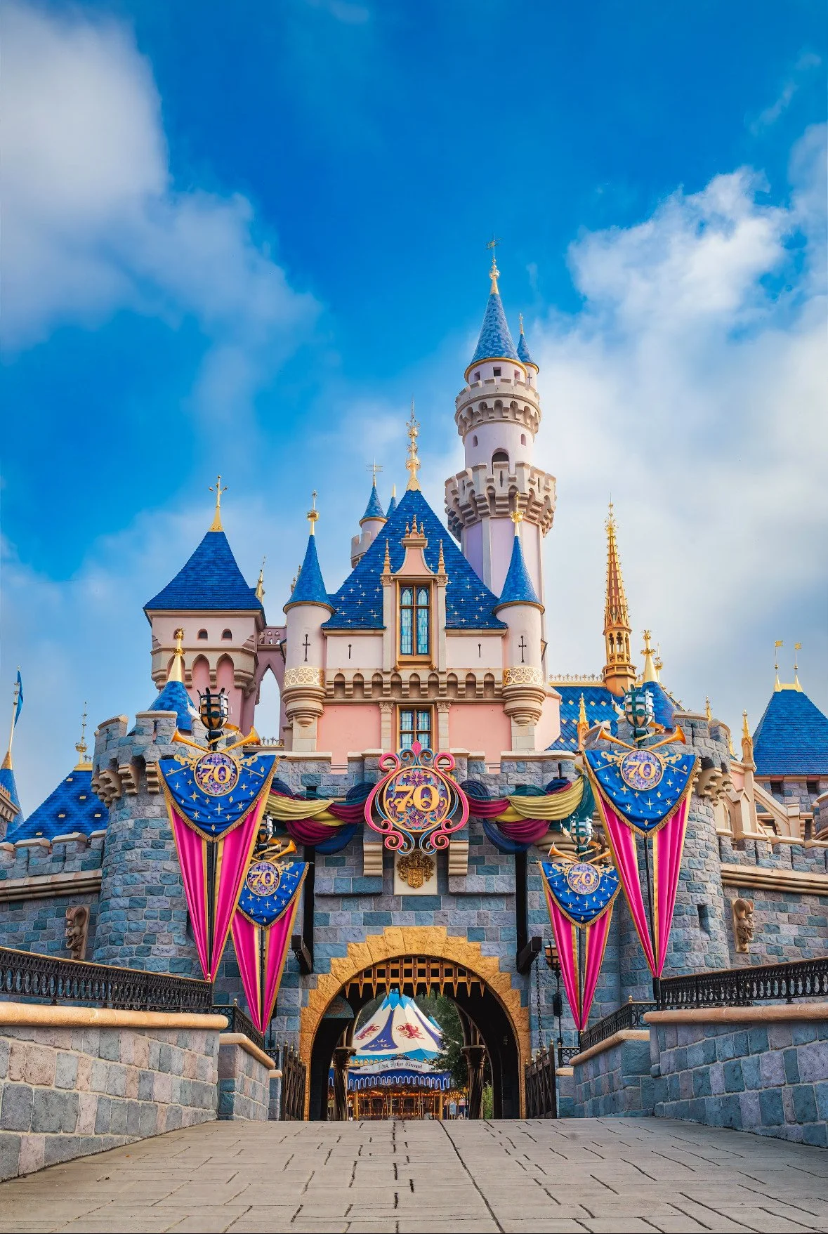 Sleeping Beauty Castle at Disneyland decorated for the 70th anniversary with banners and ornaments, under a partly cloudy sky.