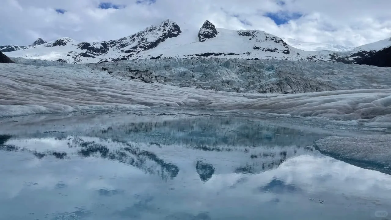 Scenic view of snow-capped mountains, a glacier, and a reflective icy lake in a cold, mountainous landscape.