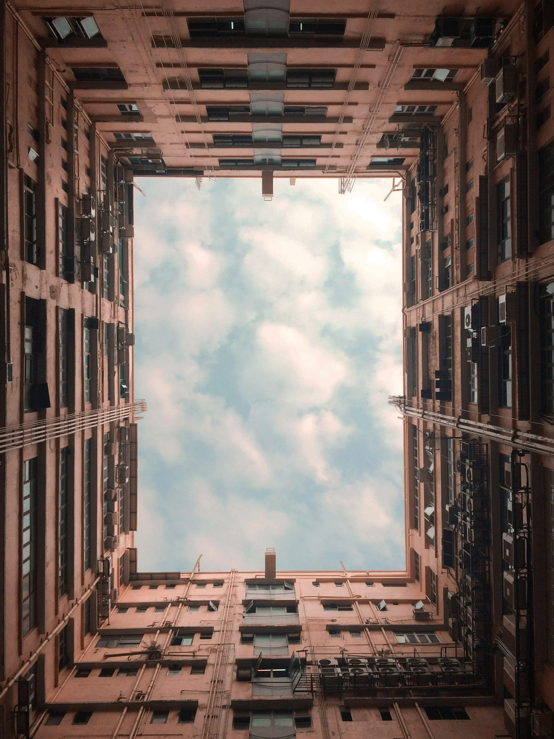 Looking up from the courtyard of an apartment building with a view of the sky surrounded by the building's walls.
