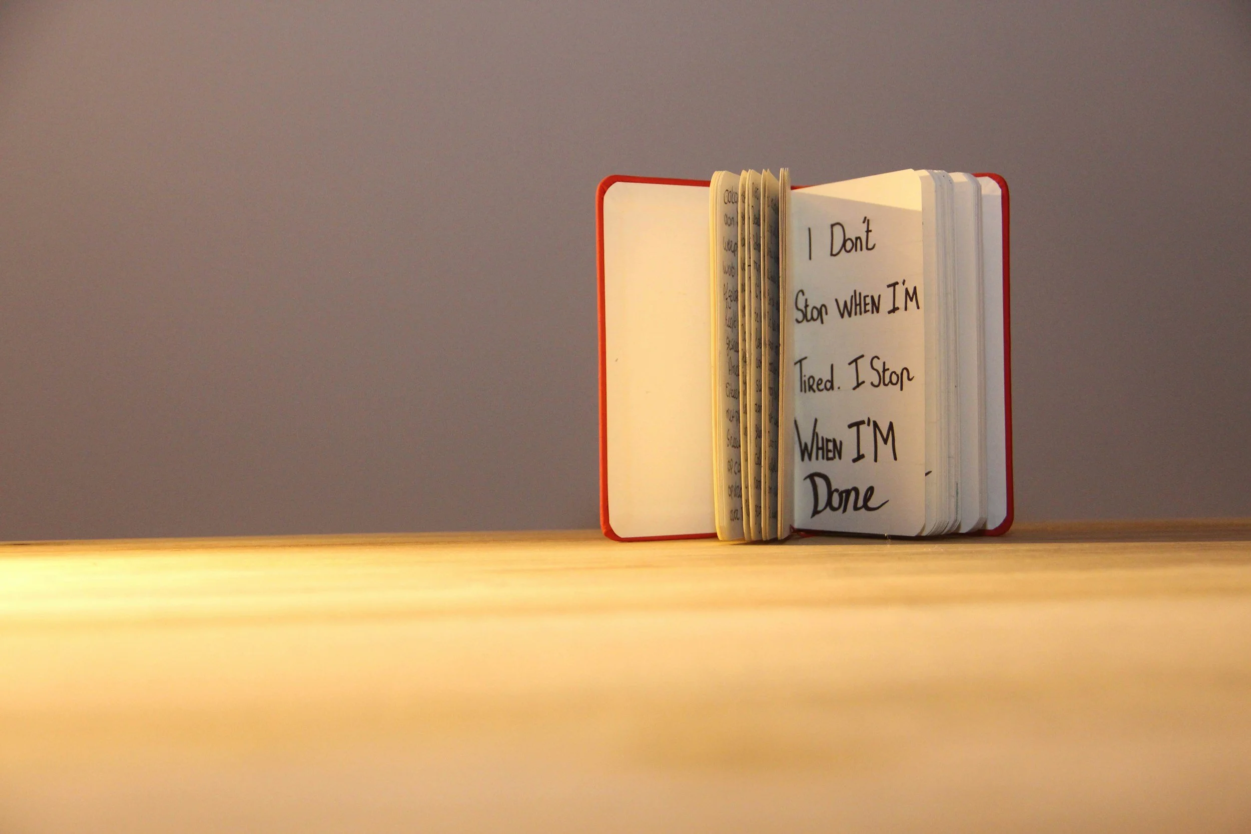 Open notebook with handwritten quote on a wooden surface, against a plain wall.
