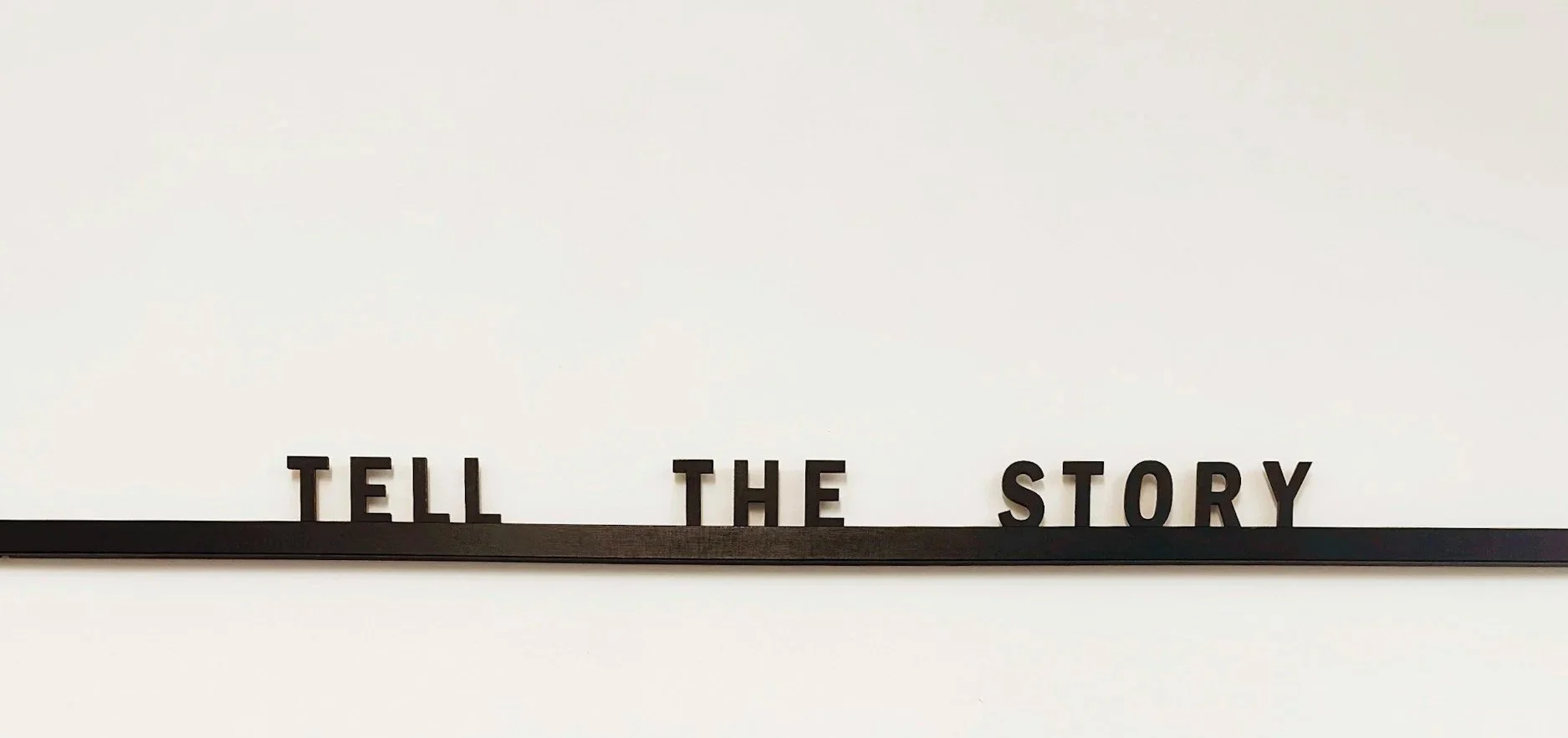 Black letters spelling out 'TELL THE STORY' on a black strip against a white background.