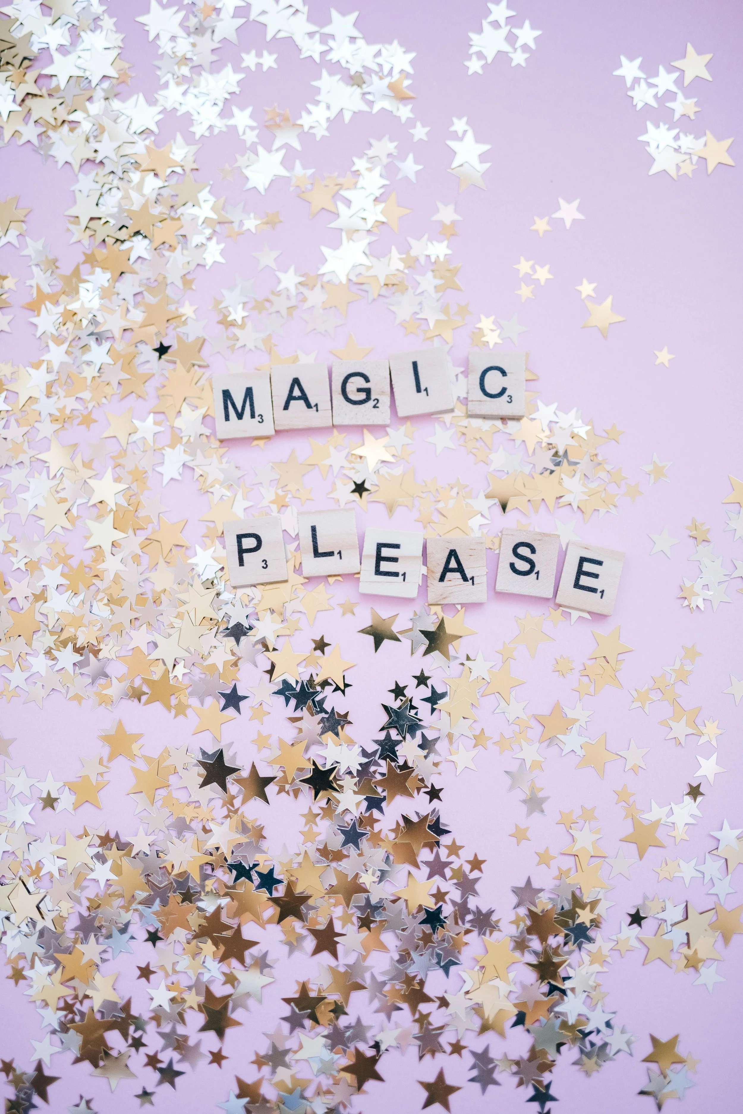 Scrabble tiles spell out 'MAGIC PLEASE' on a pink background surrounded by gold and white star-shaped confetti.