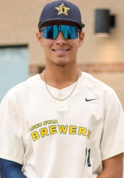 Young man wearing a baseball cap, sunglasses, and a white baseball jersey with "Lone Star Brewers" written on it, smiling outdoors.