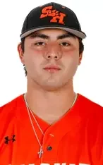 Young man wearing a black baseball cap and red sports jersey, with necklaces, against a plain background.
