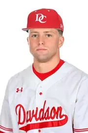 A baseball player wearing a white uniform with red accents and a red cap, featuring 'D' and 'C' logos, representing the Davidson baseball team.