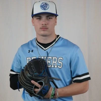Young man in baseball uniform holding a glove, wearing a cap, and standing in front of a plain background.