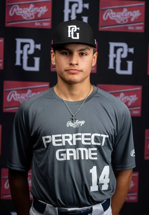 Young male baseball player wearing a gray jersey with number 14, black cap with PG logo, and silver necklace, standing in front of a backdrop with logos.
