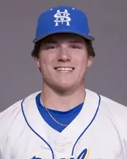 Young baseball player wearing a blue cap and white uniform with blue accents, smiling.