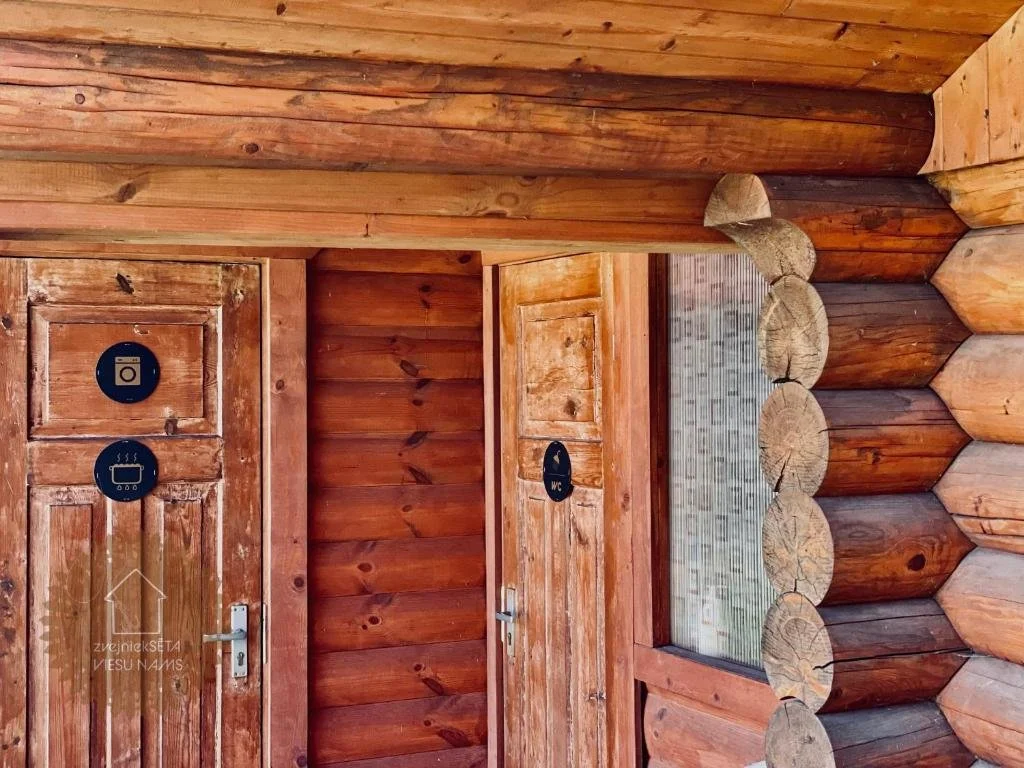 Wooden walls and ceiling of a rustic bathroom or sauna area with signs indicating washing machine, hot tub, and toilet.