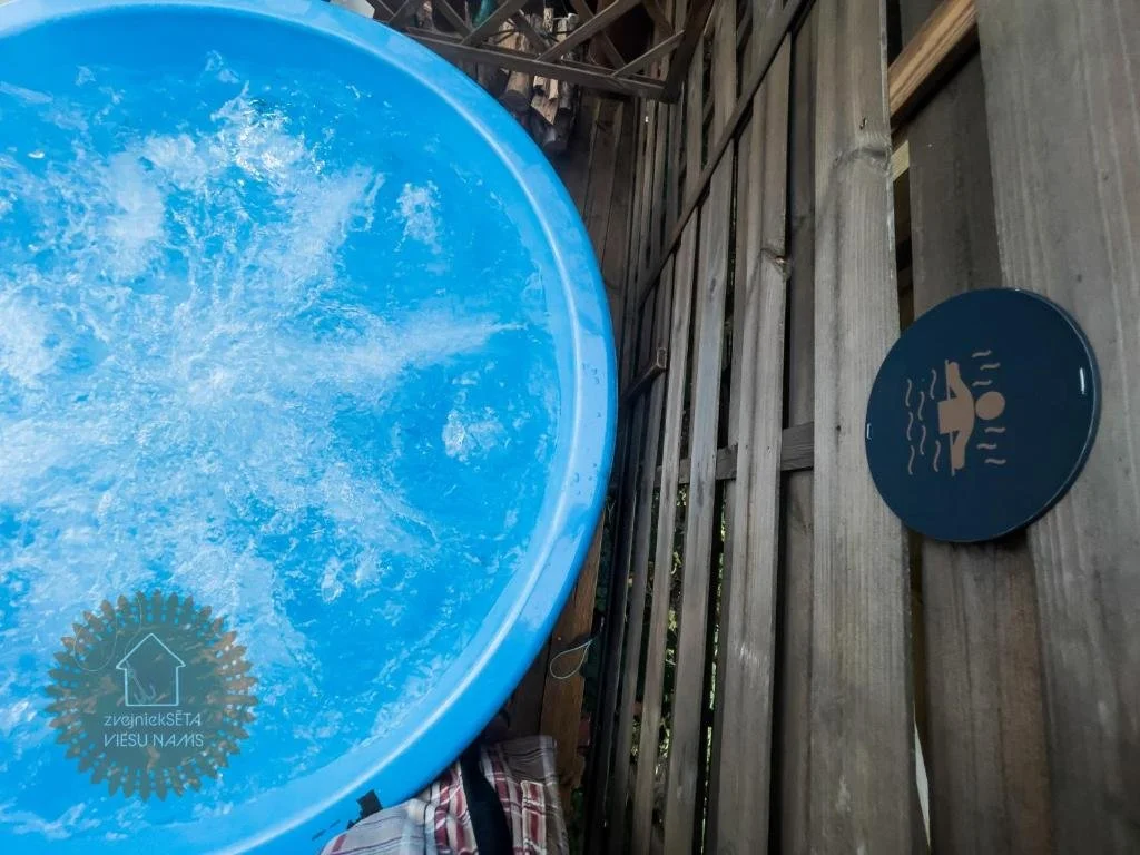 Blue inflatable hot tub with water jets bubbling, surrounded by wooden fencing, with a round blue sign depicting a person relaxing in a hot tub.