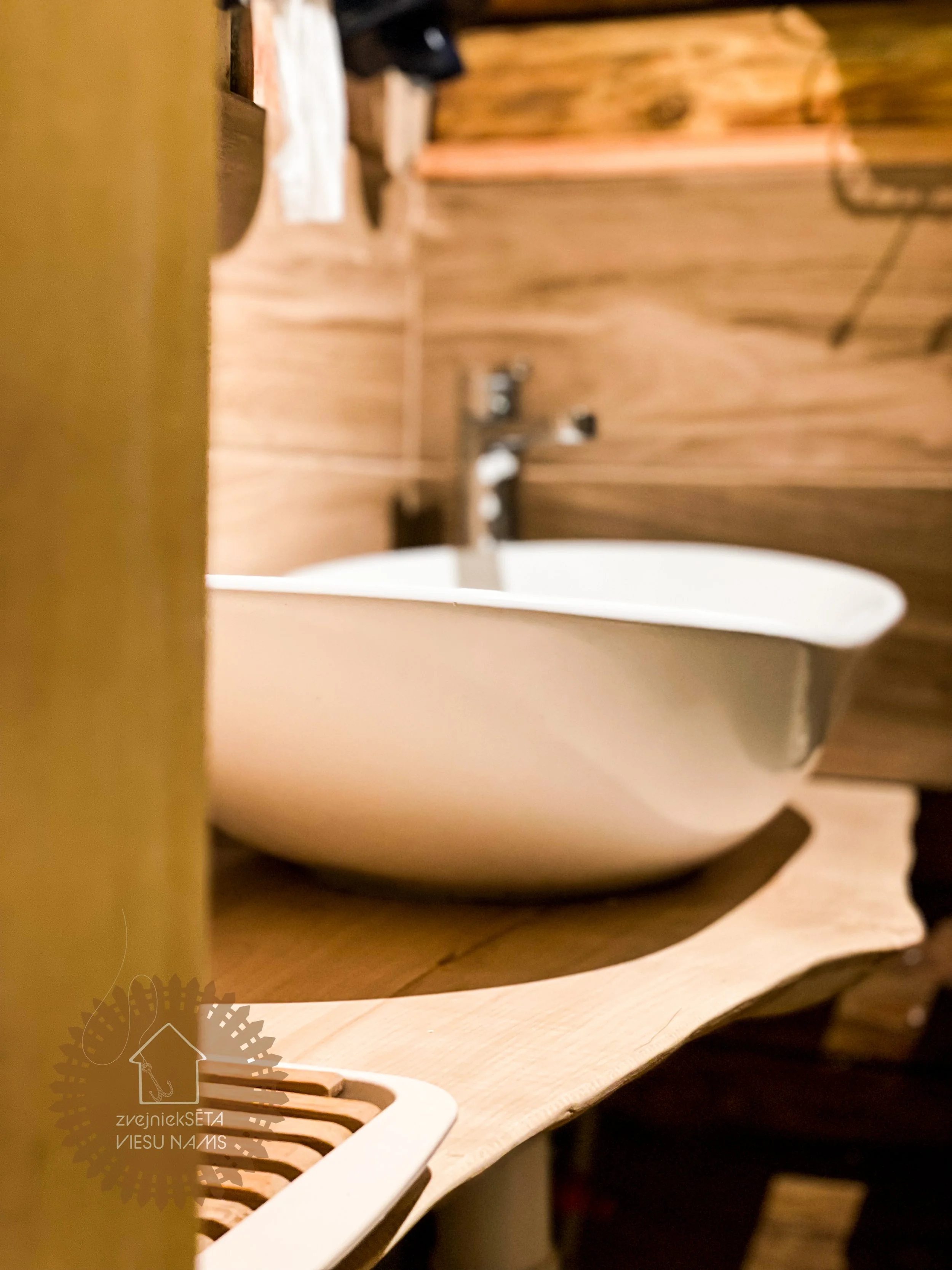 Close-up view of a white ceramic sink on a wooden countertop with a wooden wall in the background.